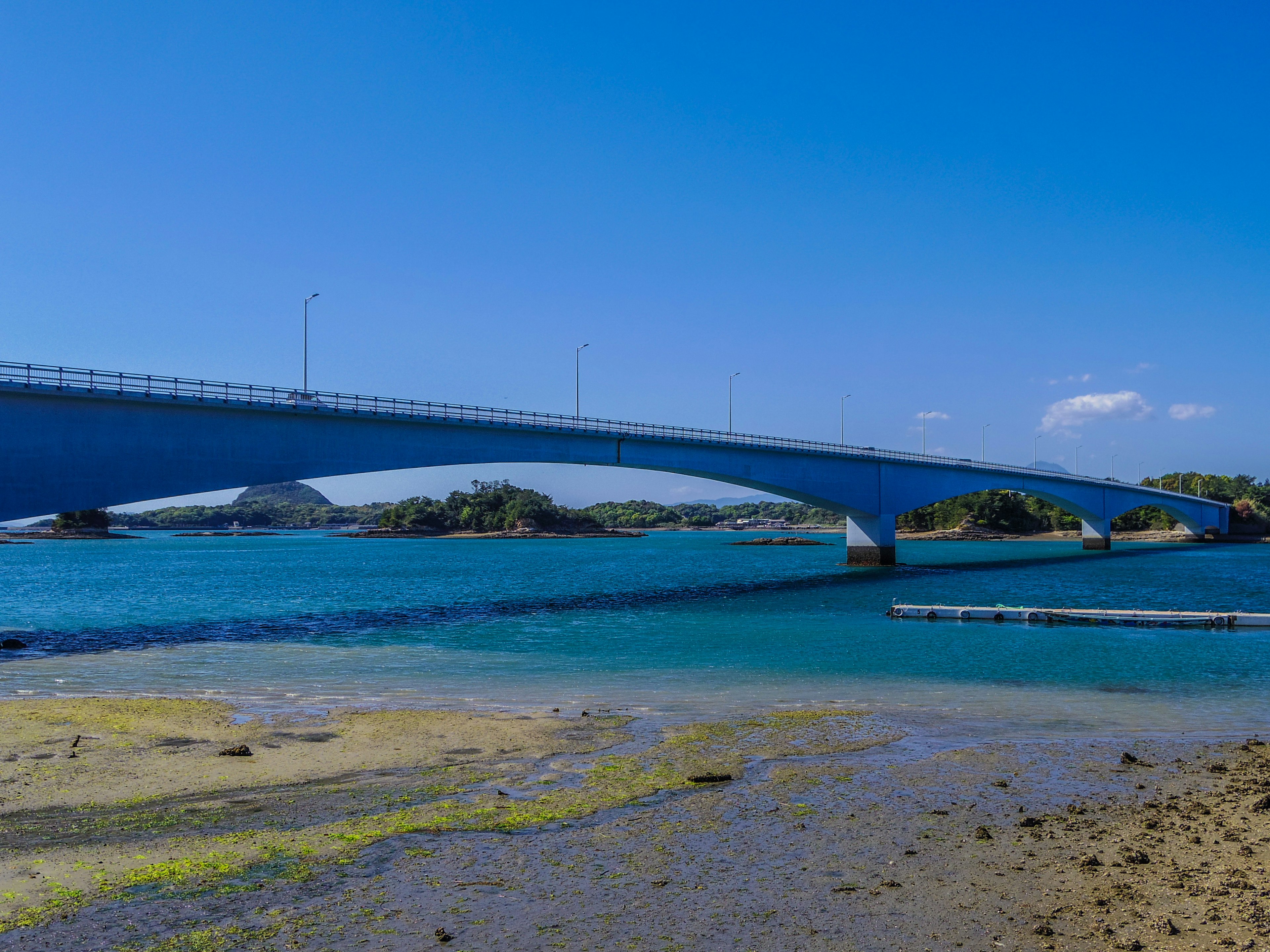 Malersicher Blick auf eine Brücke unter einem blauen Himmel mit klarem Wasser darunter und einem Sandstrand