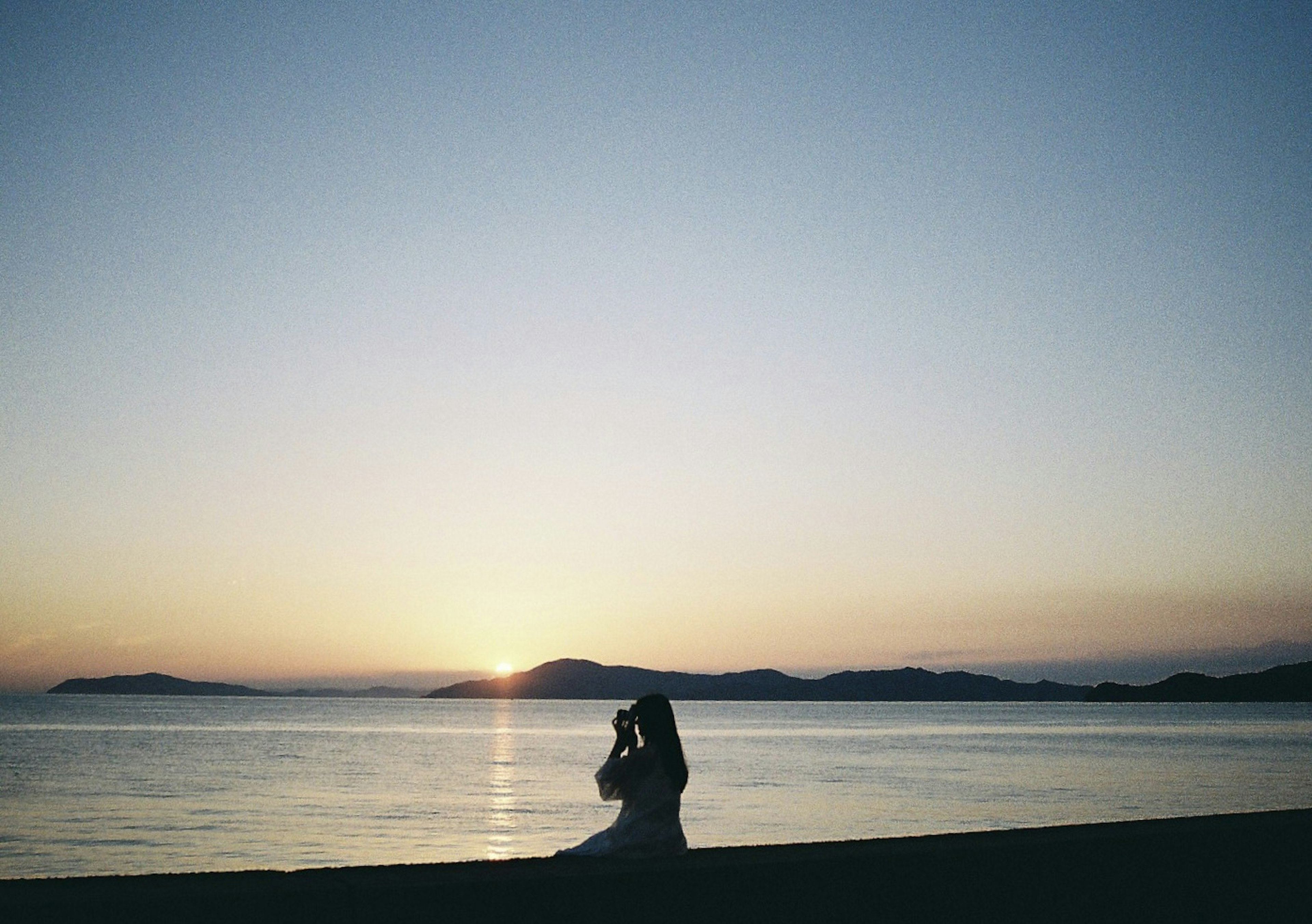 夕日を背にしたカップルが海辺で抱き合っている