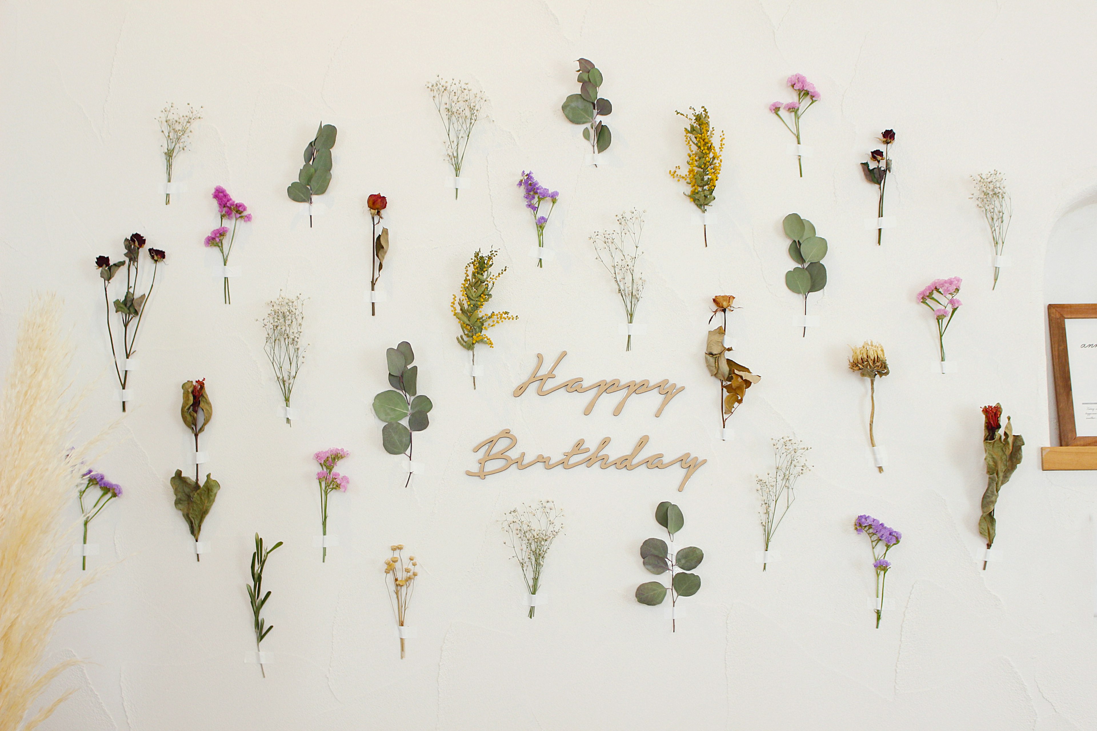 Pared decorada con flores secas y el texto Feliz Cumpleaños