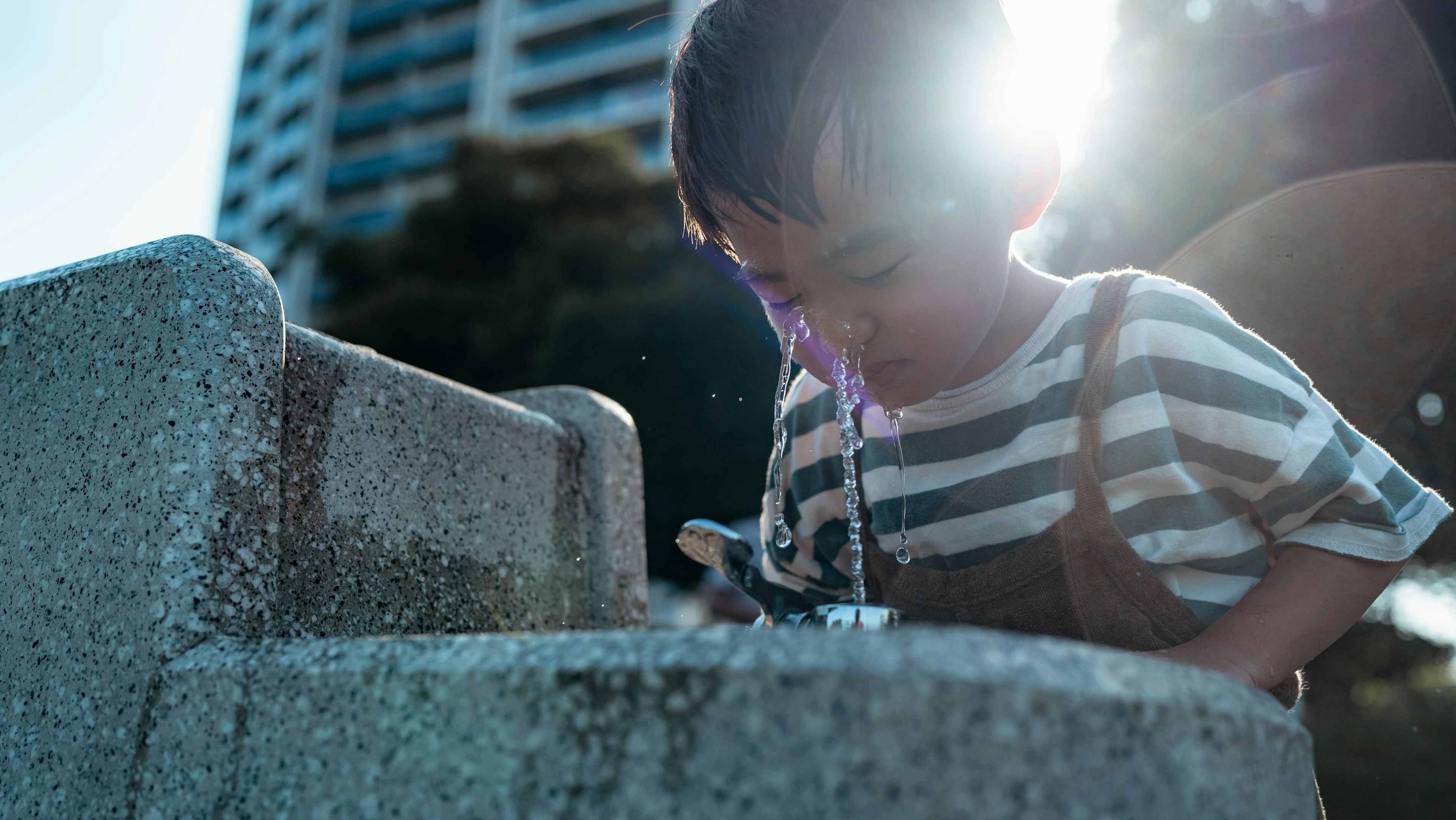 Un garçon buvant à une fontaine avec la lumière du soleil derrière lui