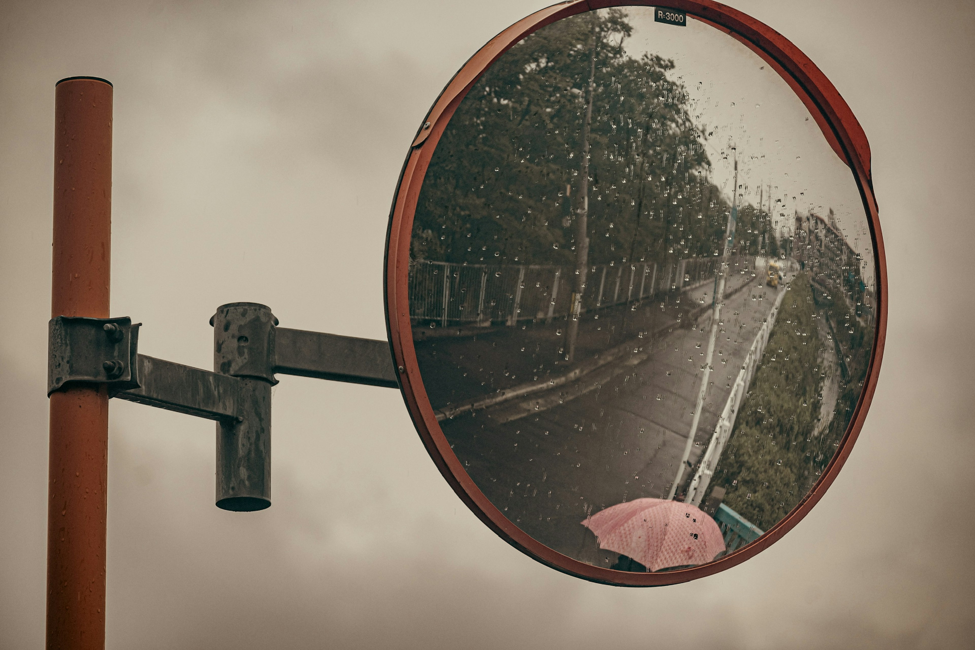 Espejo rojo que refleja una carretera lluviosa y un paraguas