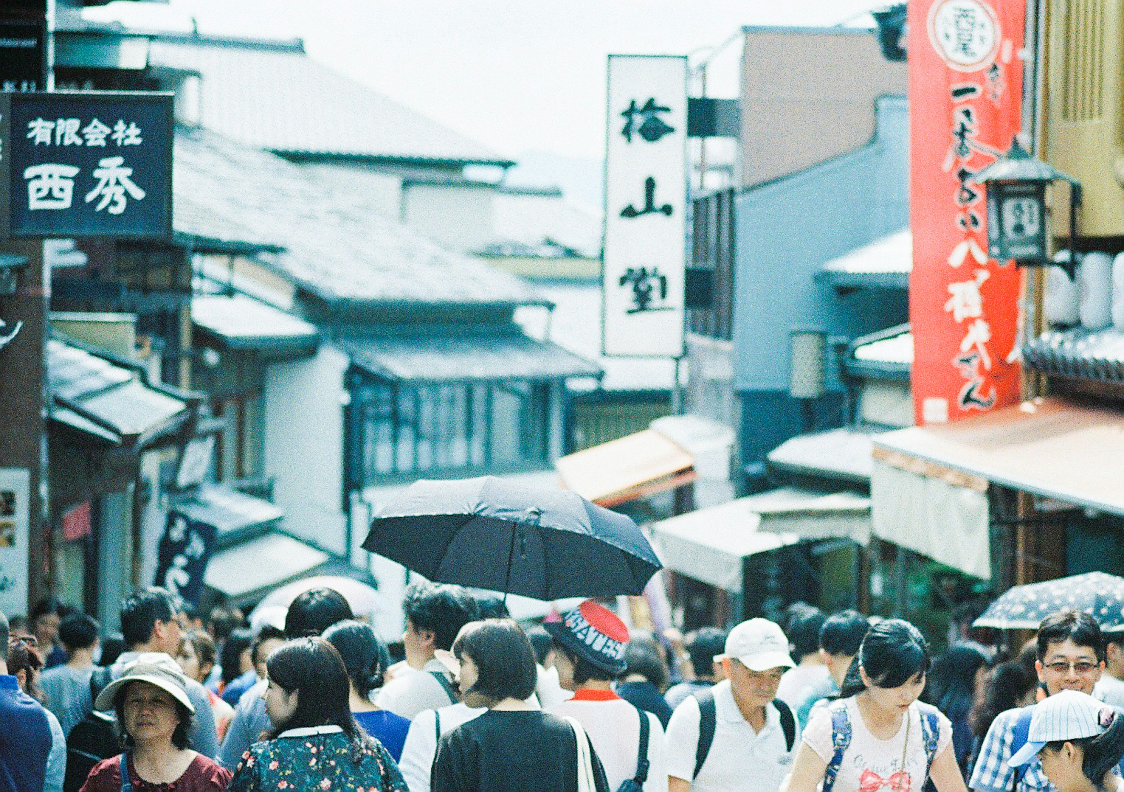 A bustling street scene with many people holding umbrellas and traditional signs