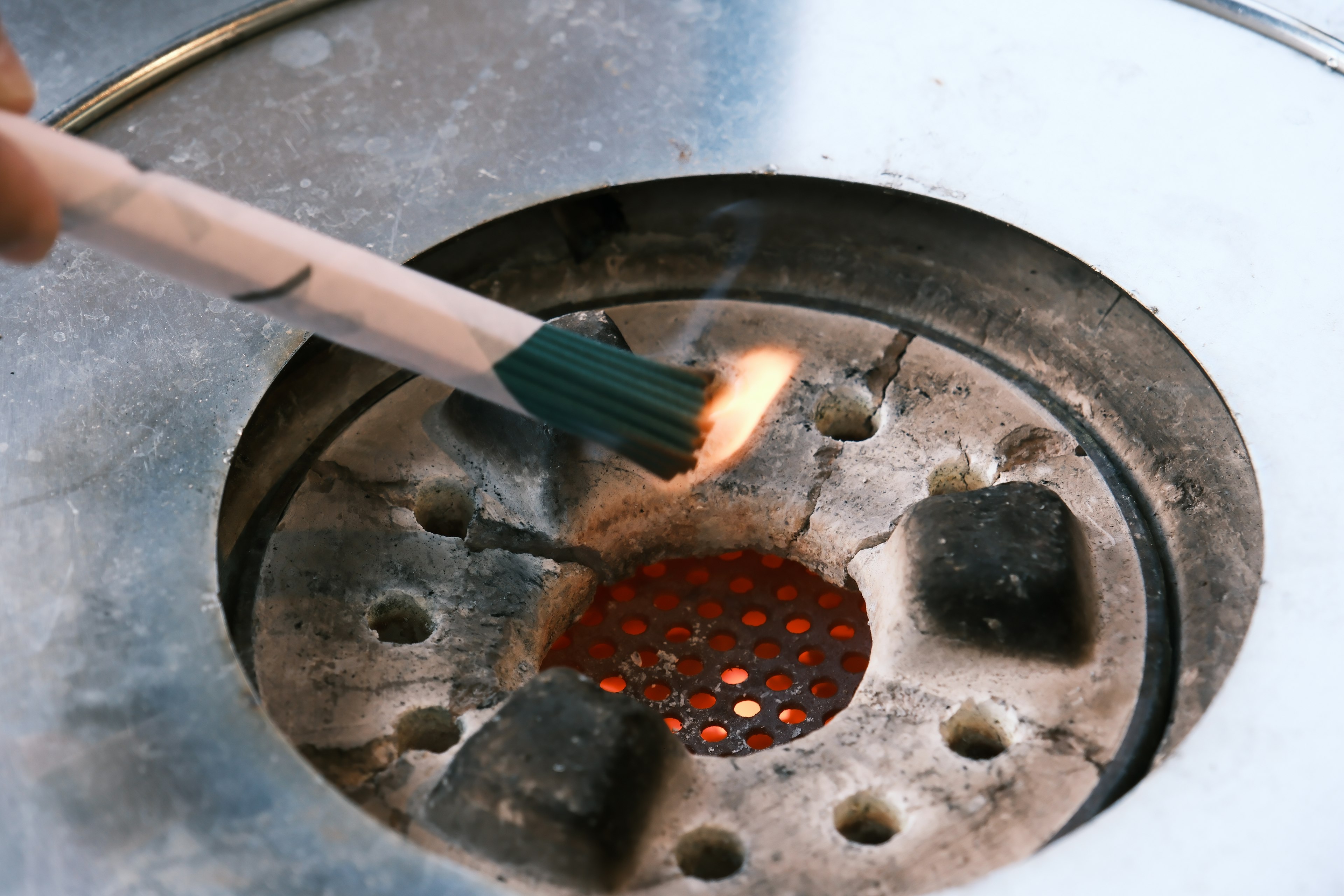 A hand holding a brush igniting a grill with glowing coals