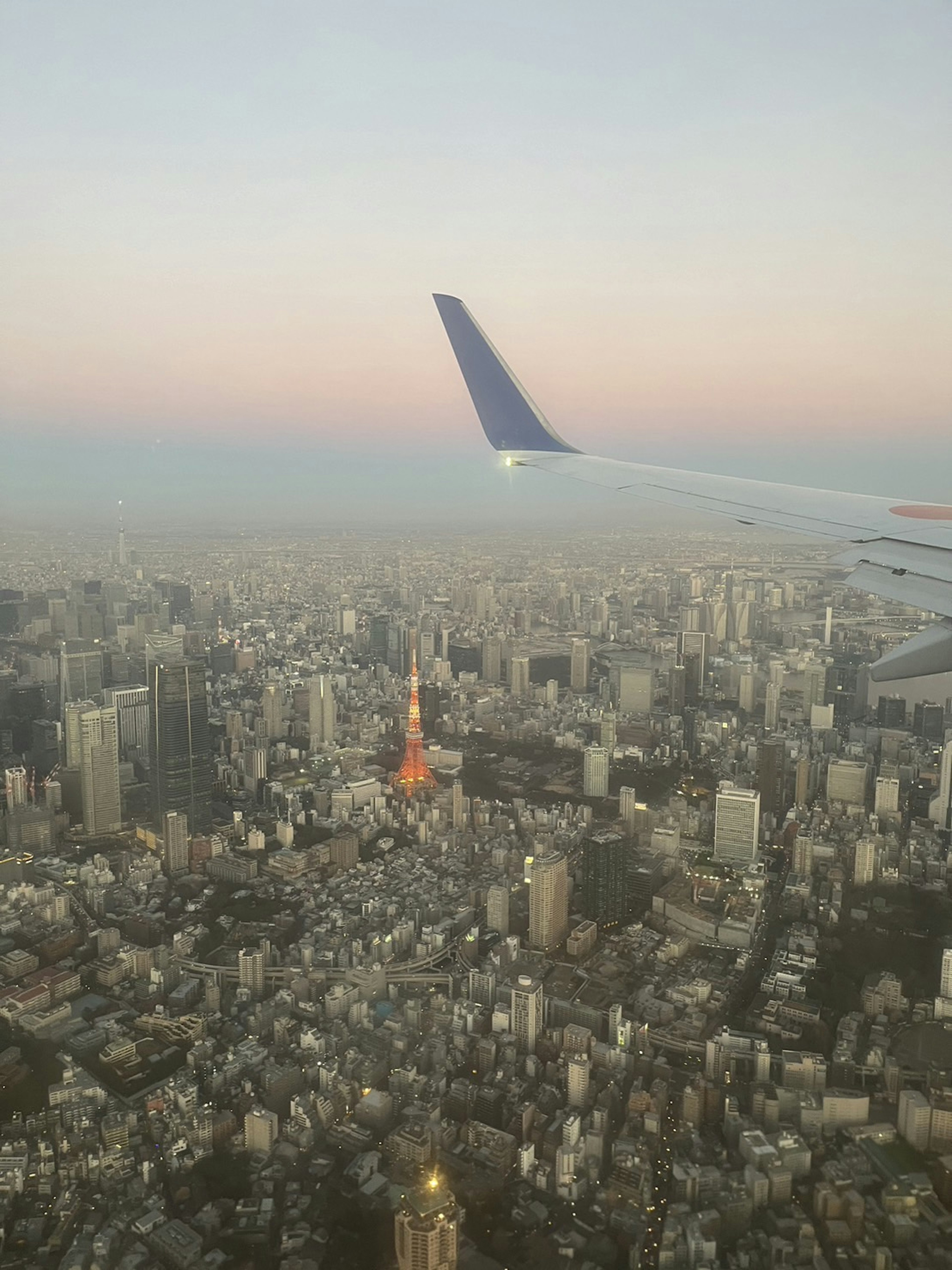 Aerial view of Tokyo at dusk with an airplane wing in the frame