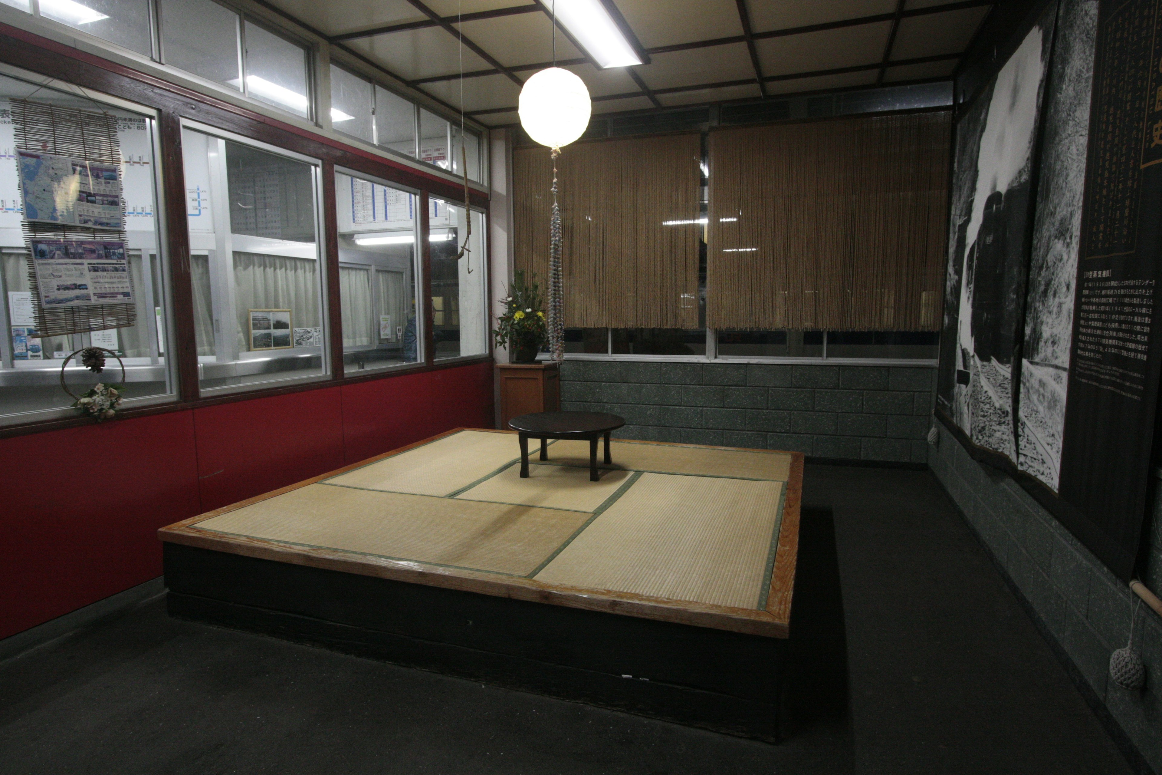 Una habitación de estilo japonés minimalista con una mesa y una silla de madera, iluminación brillante, paredes rojas y luz natural de las ventanas