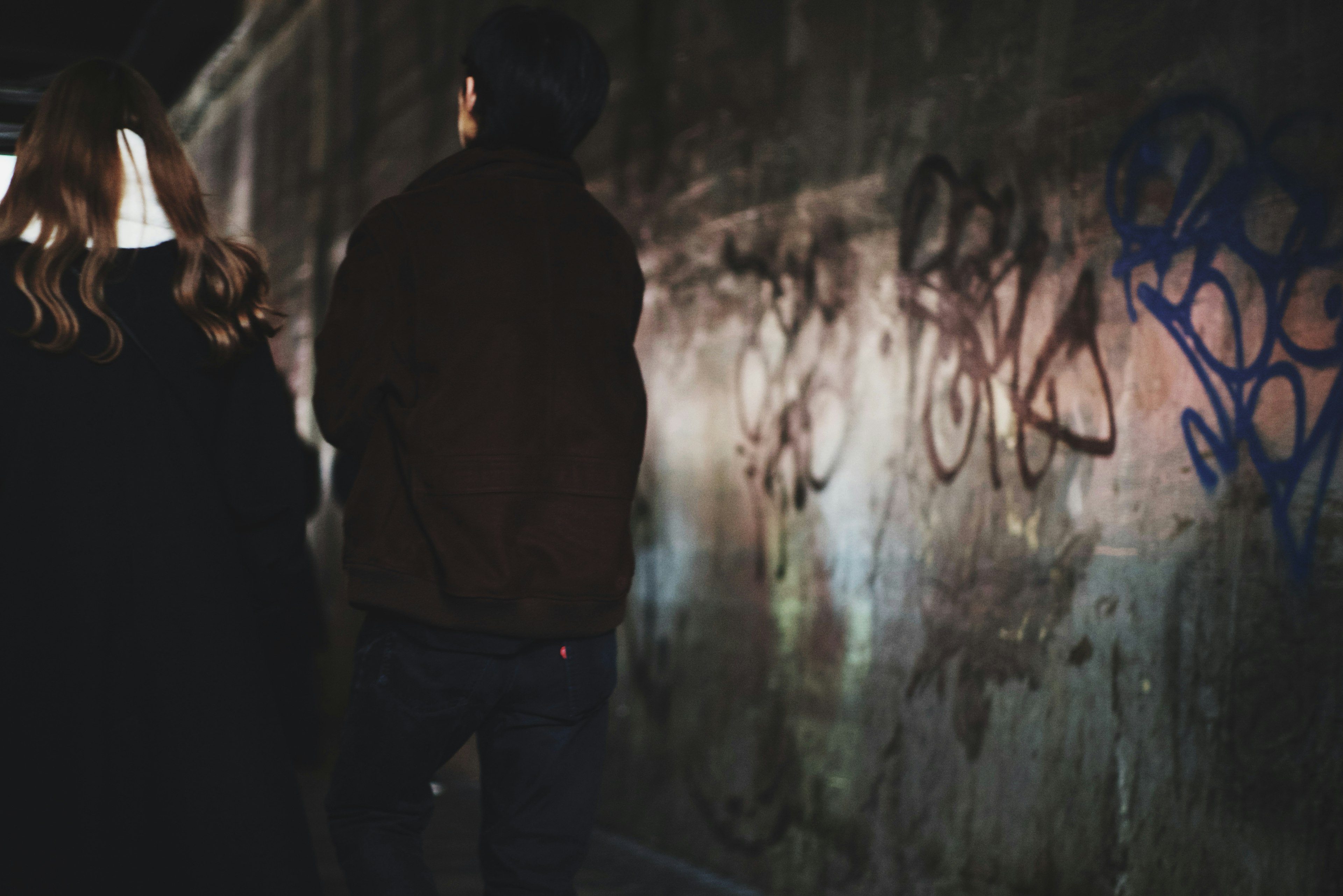 Zwei Figuren gehen in einer schwach beleuchteten Gasse mit bunten Graffiti an der Wand