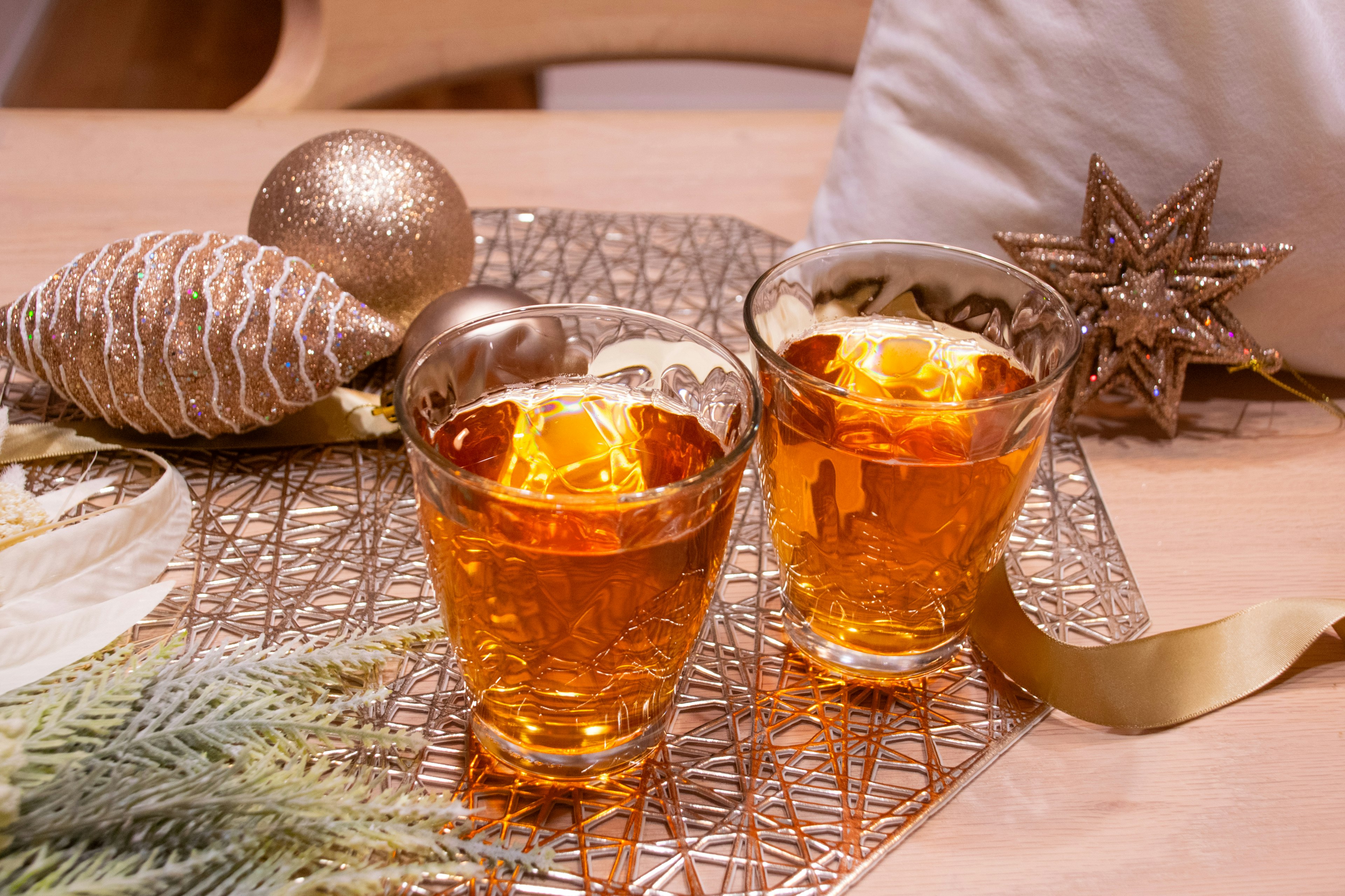 Two glasses of amber drink with Christmas decorations on the table