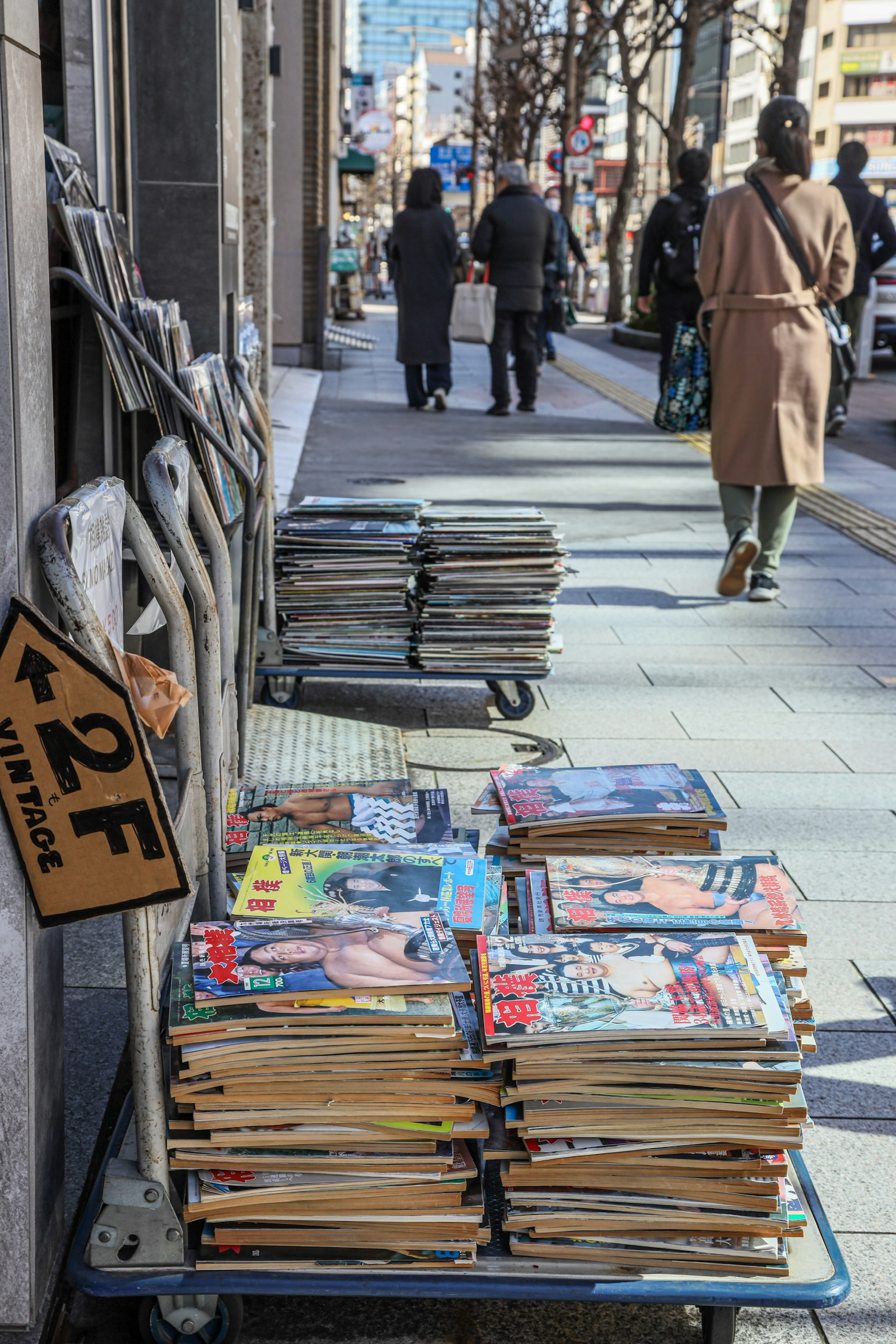 雑誌が積まれた屋外の販売台と通行人の姿