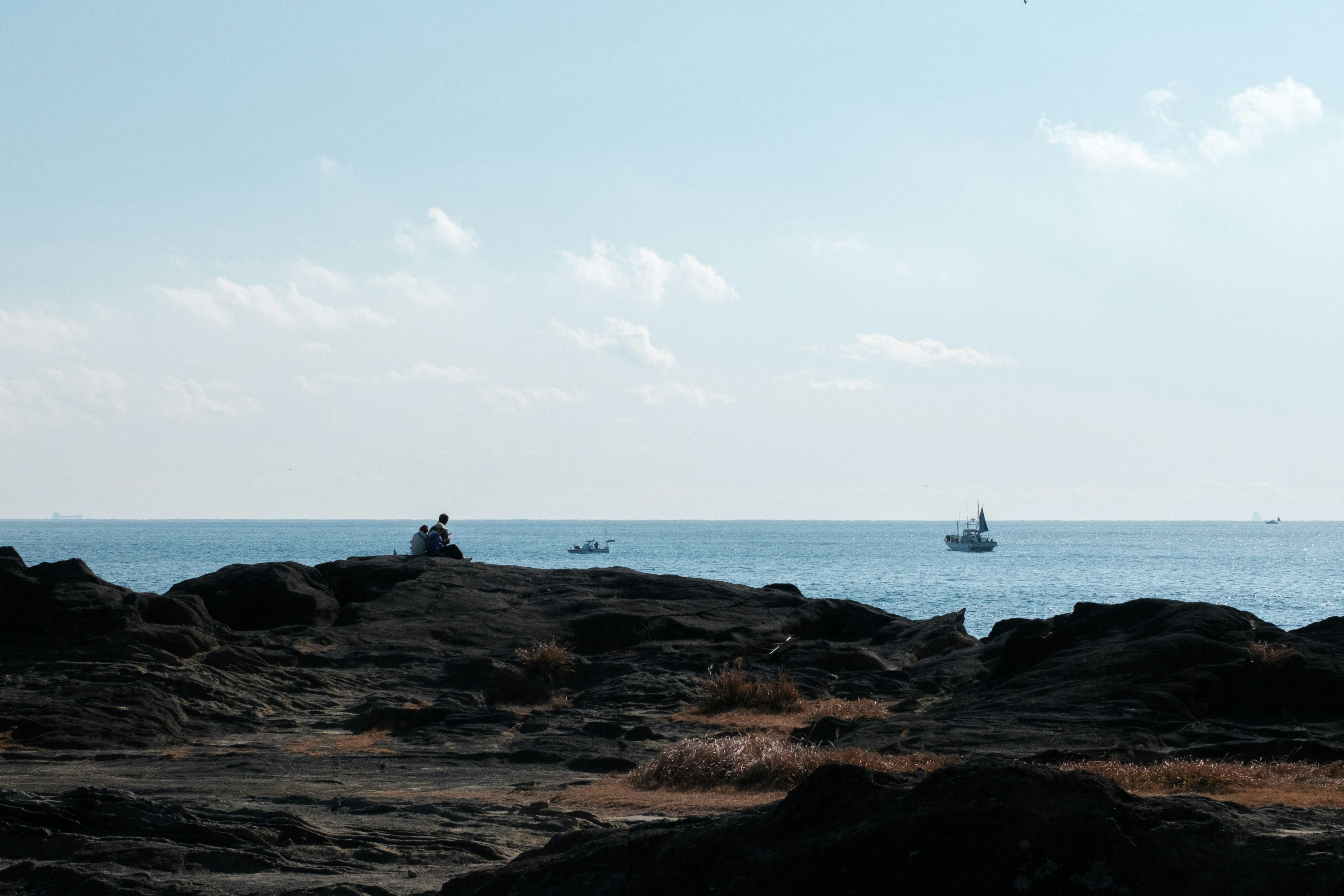 Une personne assise sur des rochers avec des bateaux dans l'océan