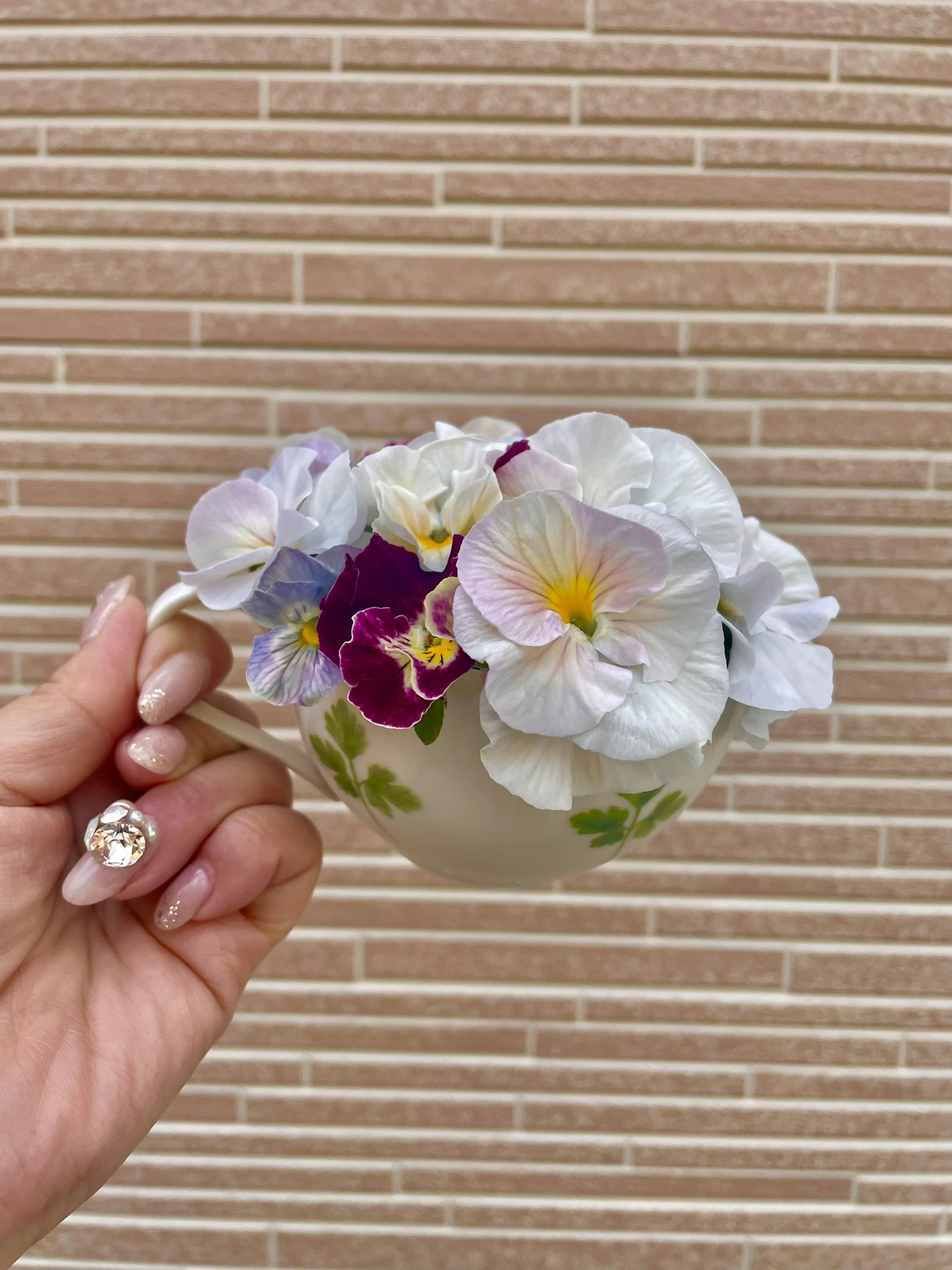 Une main tenant une tasse remplie de fleurs colorées comprenant des fleurs blanches et violettes