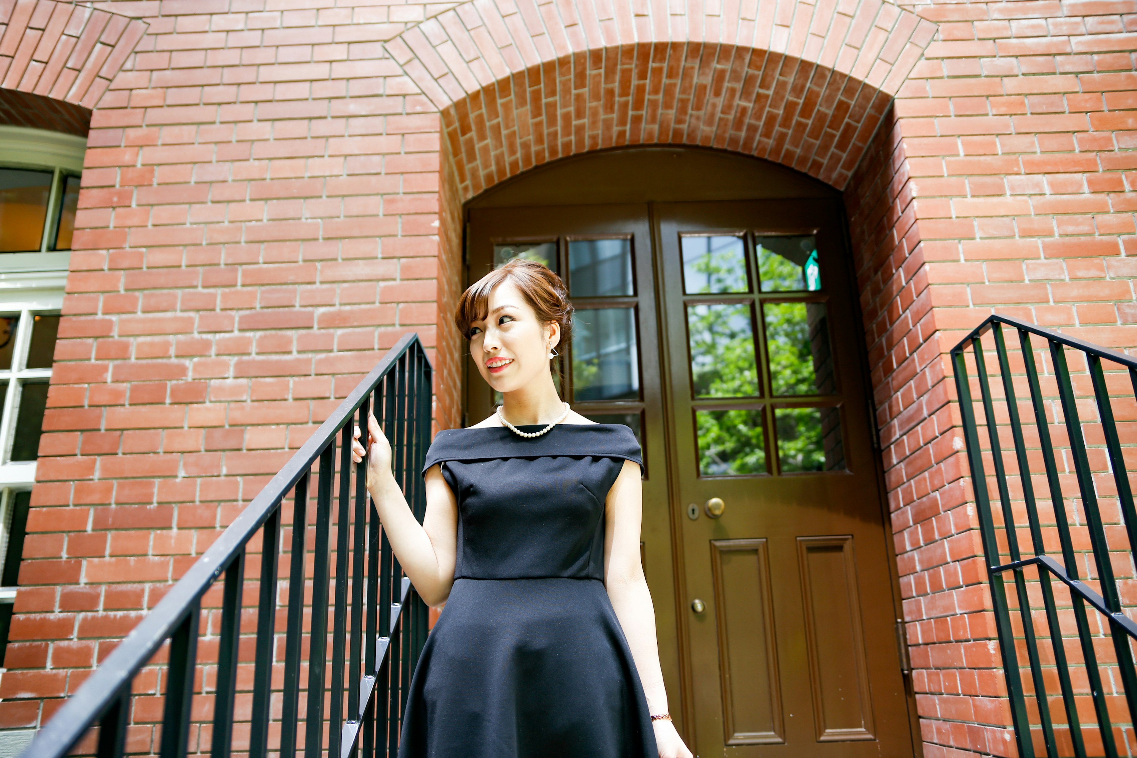 A woman in a black dress standing in front of a brick building