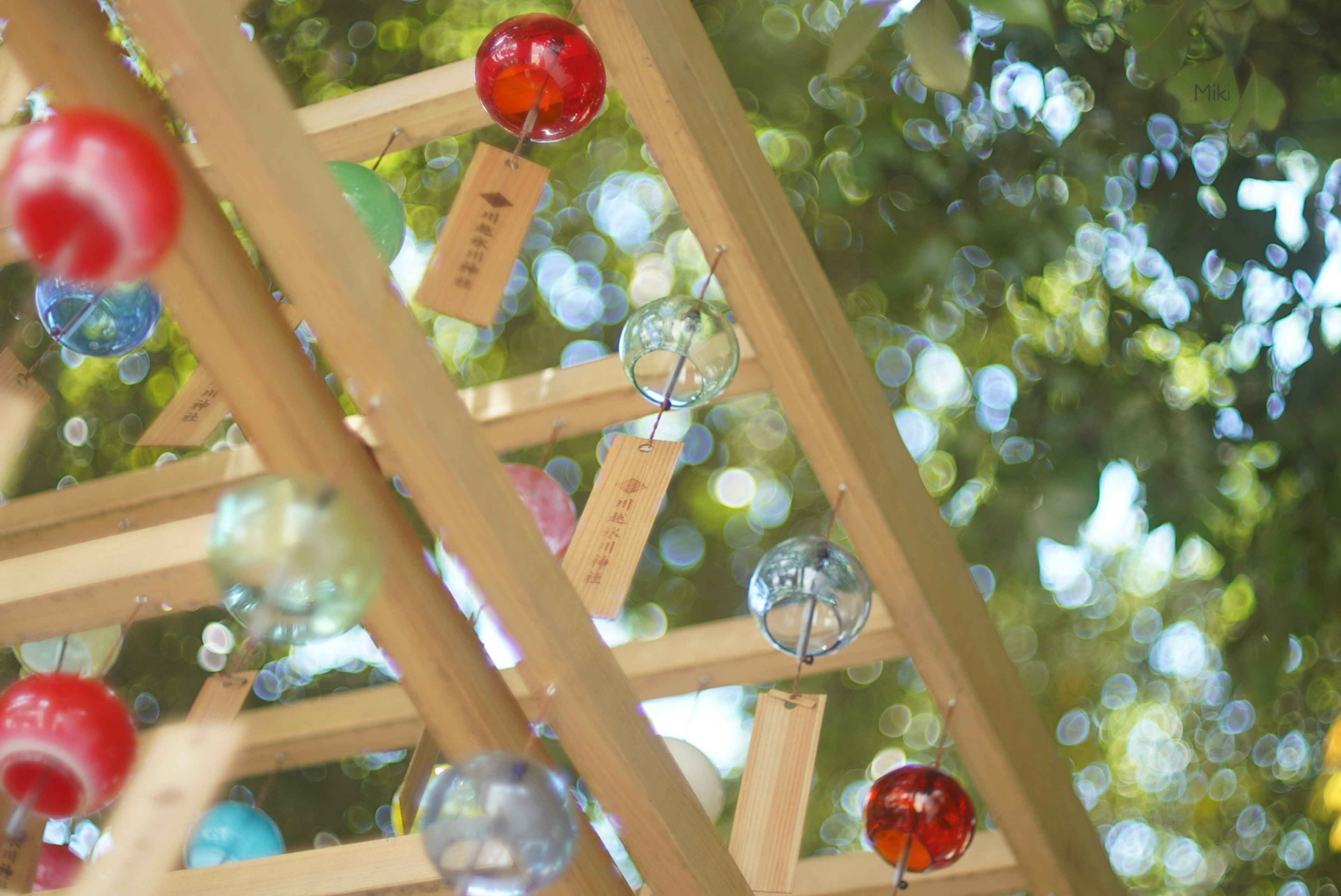 Bunte Glasperlen hängen an einer Holzstruktur umgeben von Grün