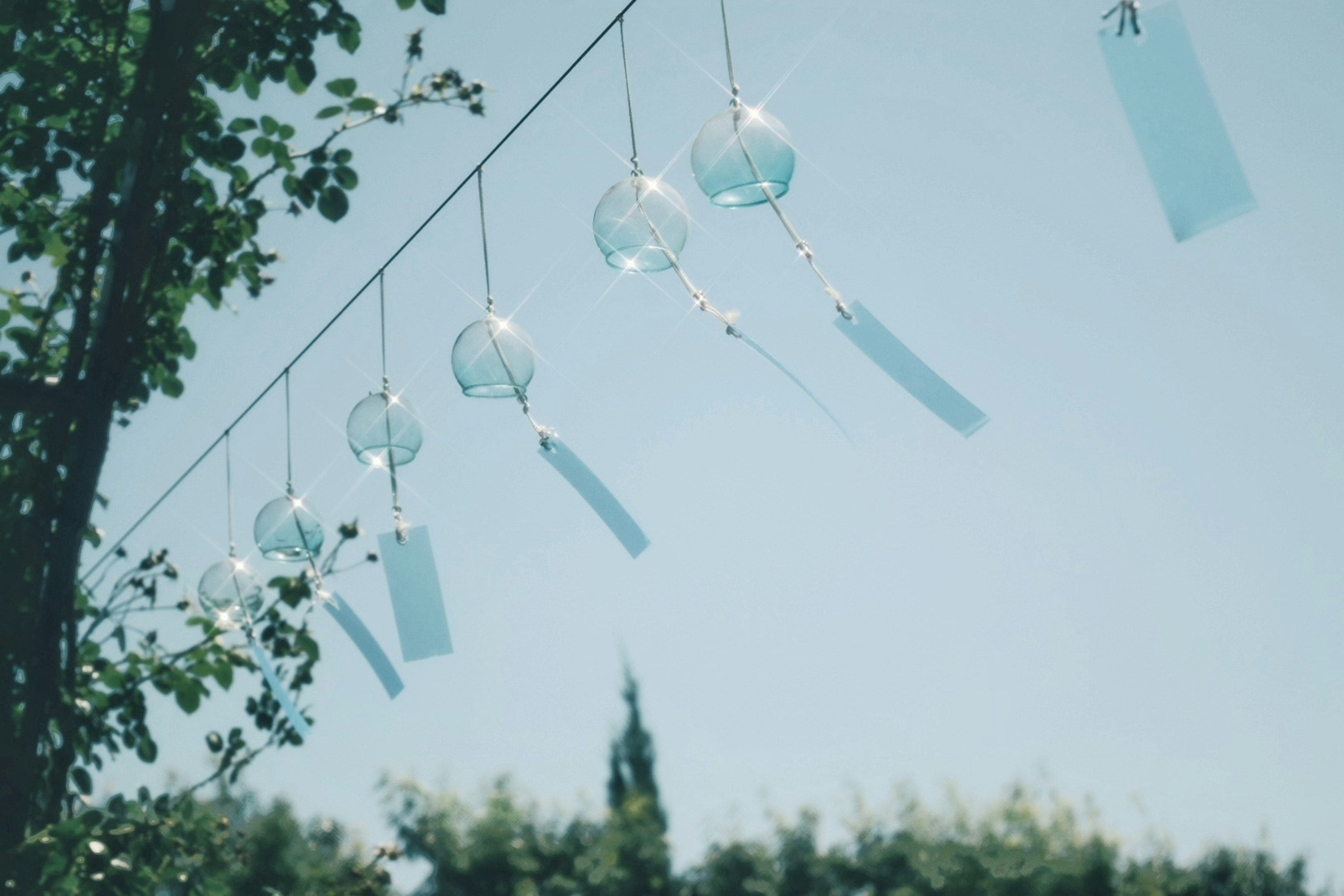 Escena de campanas de viento balanceándose bajo un cielo azul con plantas al fondo