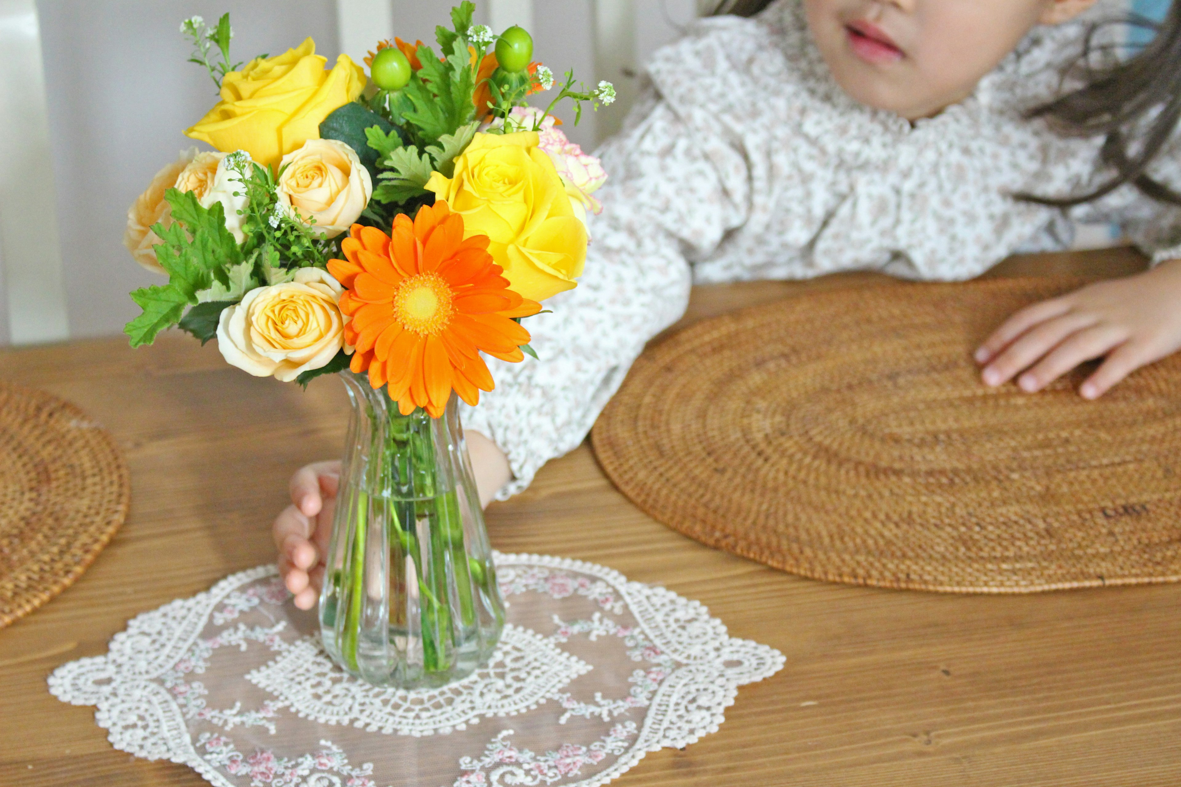 Un niño alcanzando un jarrón con flores coloridas sobre una mesa de madera