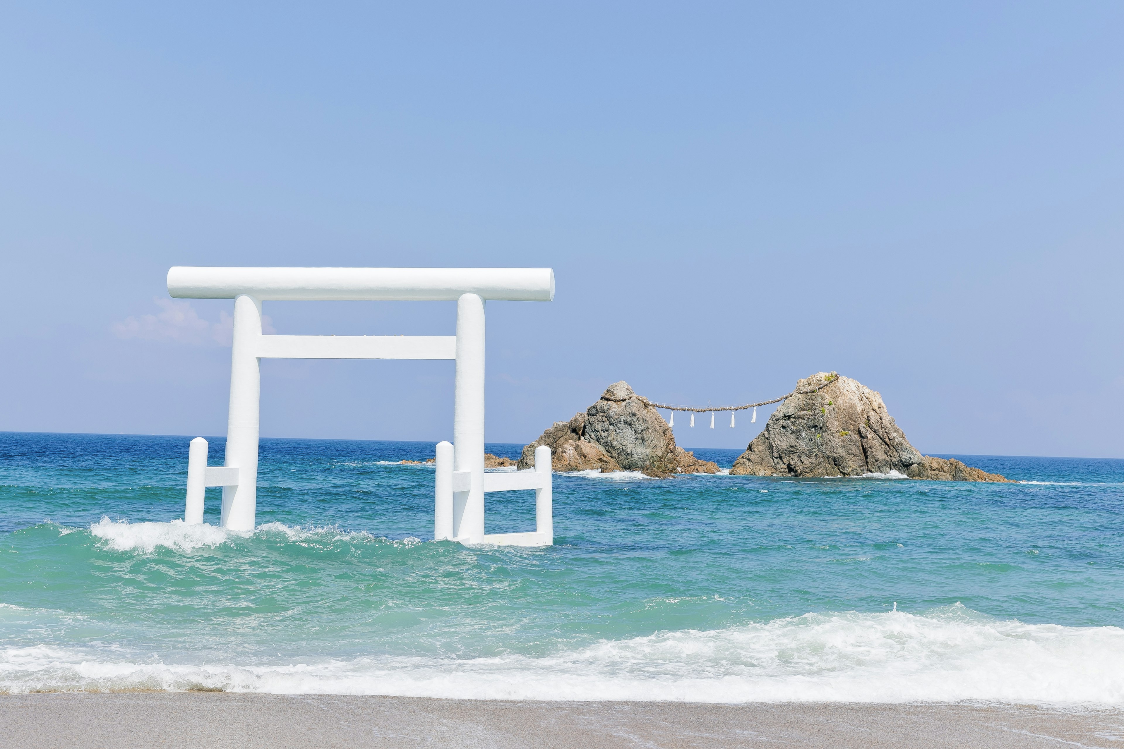 A white torii gate floating in the sea with rocky formations in the background