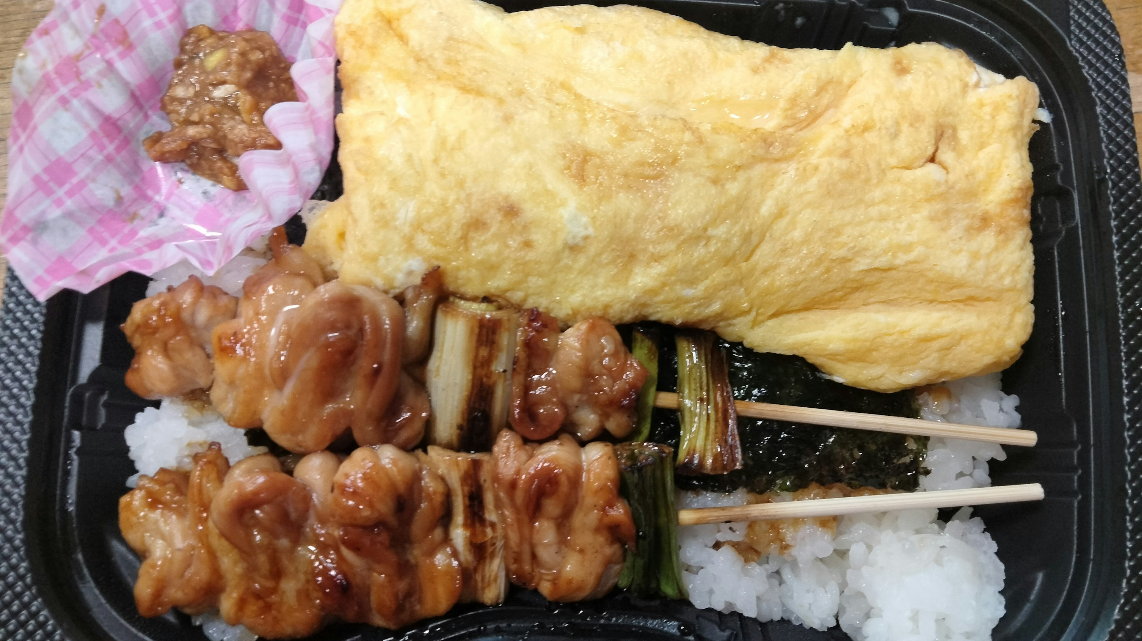 Caja bento con brochetas de pollo a la parrilla y una tortilla servida con arroz