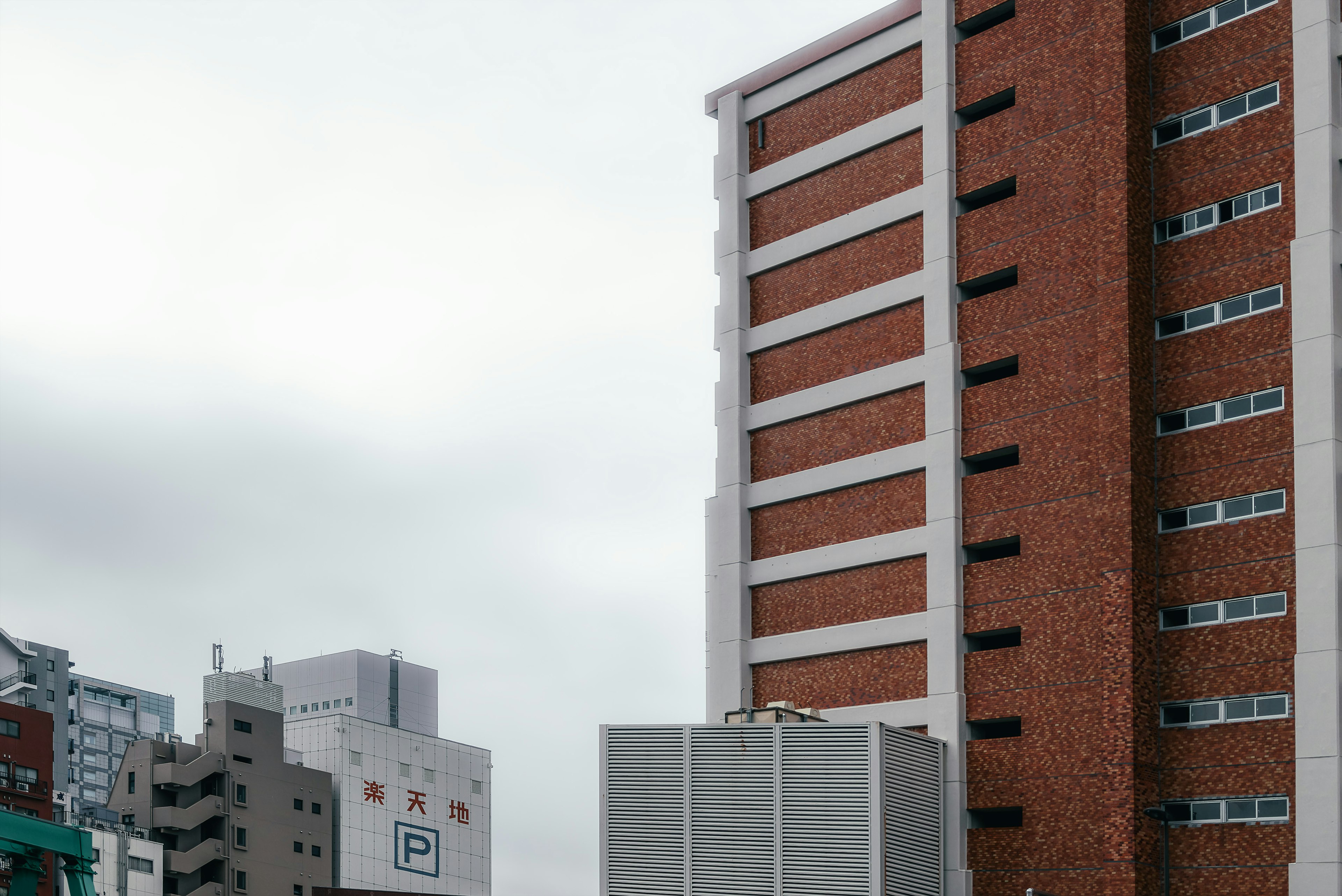 Red brick building under a gray sky with nearby modern structures