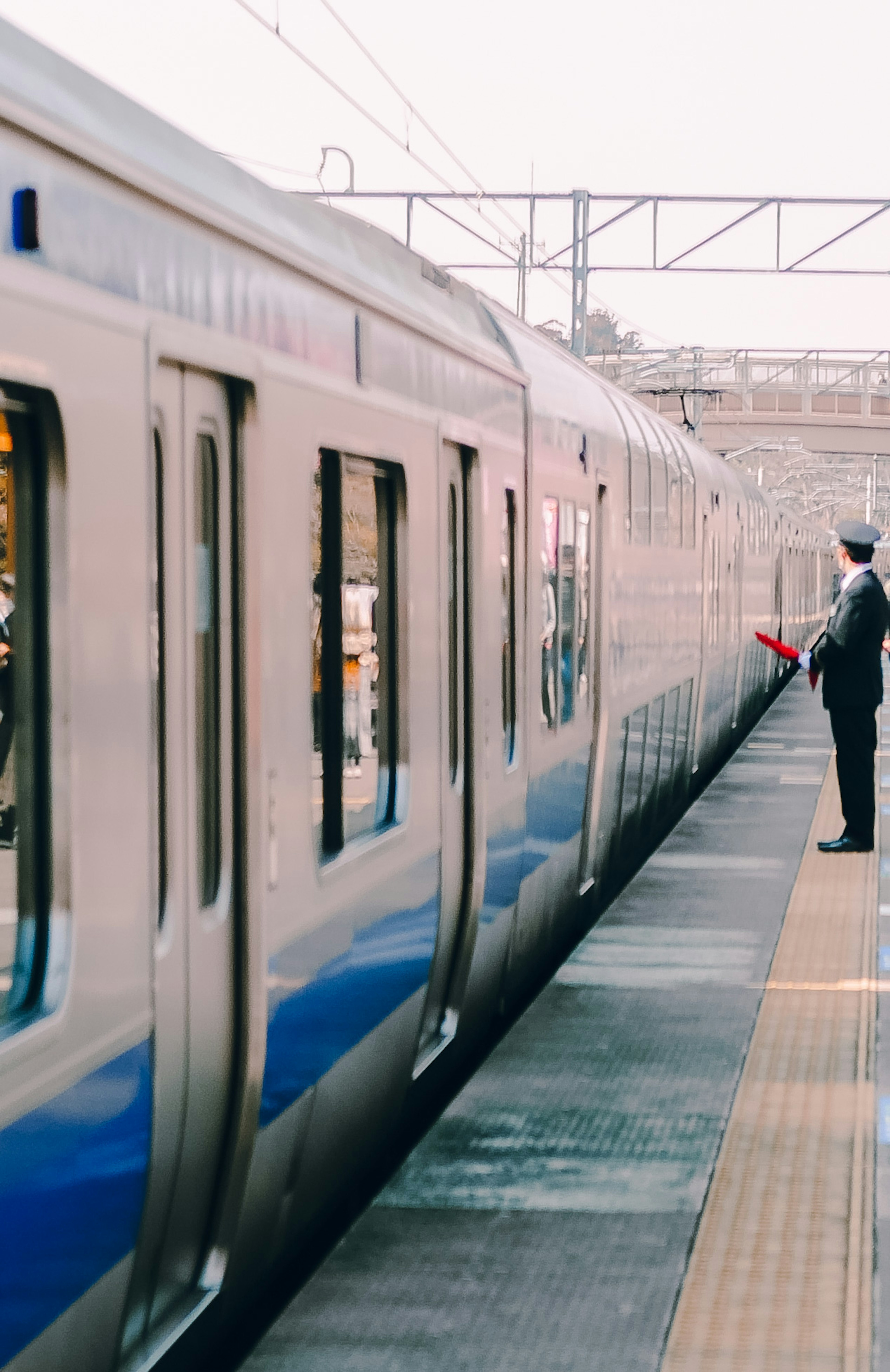 Blue train with a station attendant waving at the platform