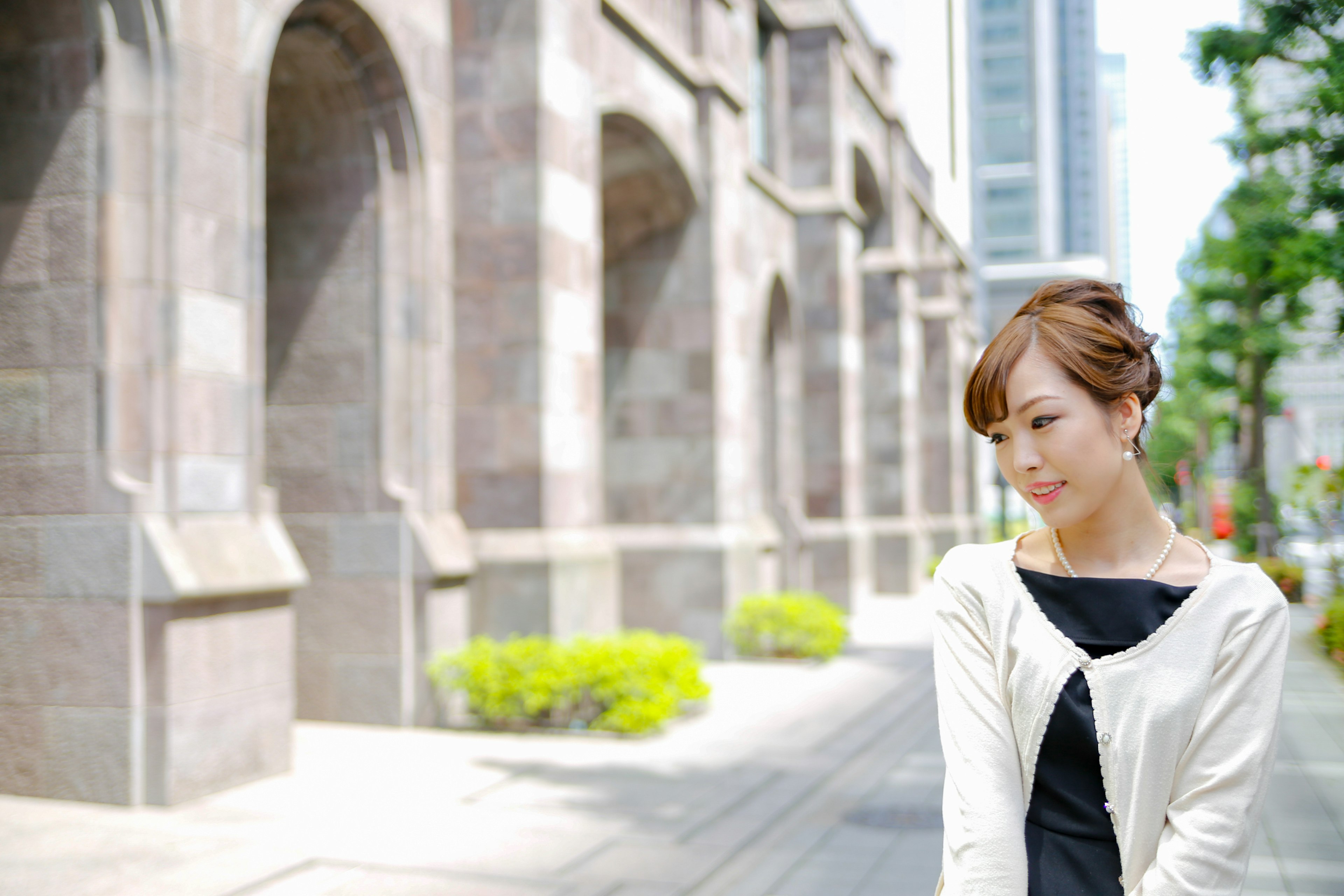 Una mujer sonriendo en la ciudad con edificios modernos y arcos de piedra al fondo