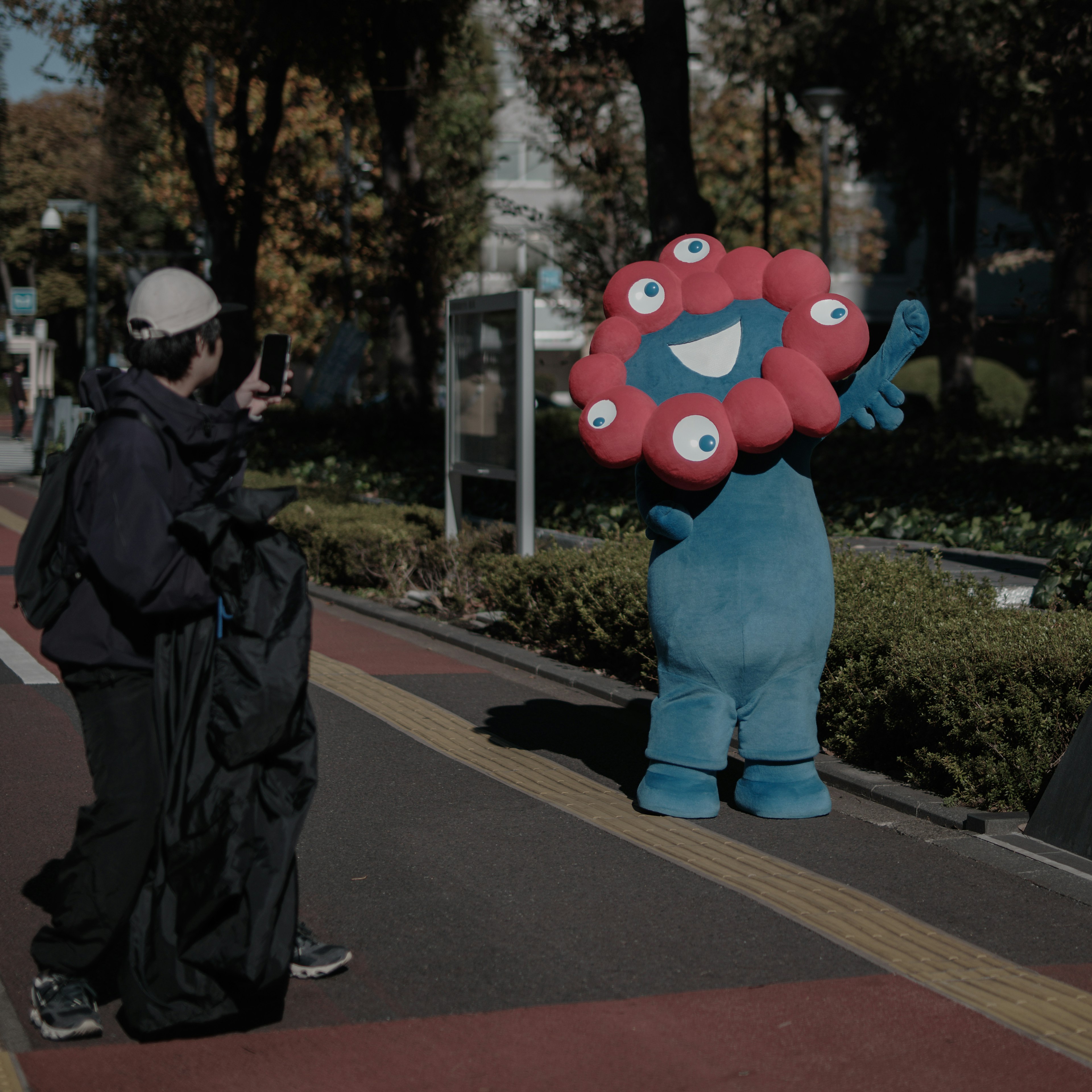 Personnage bleu avec une tête rouge en forme de fleur saluant sur le trottoir