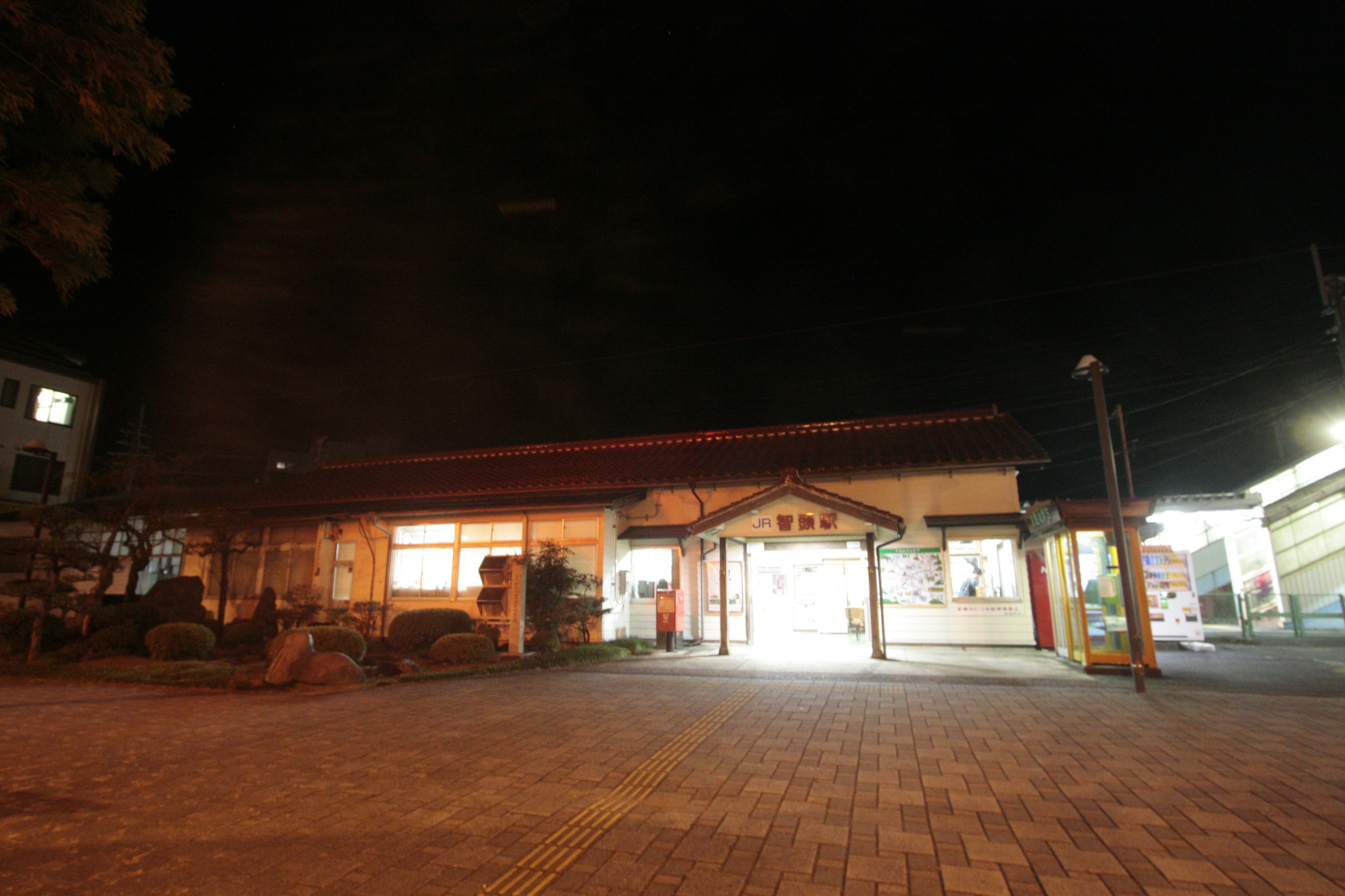 Night view of a train station building with a bright entrance surrounded by streetlights and a quiet atmosphere