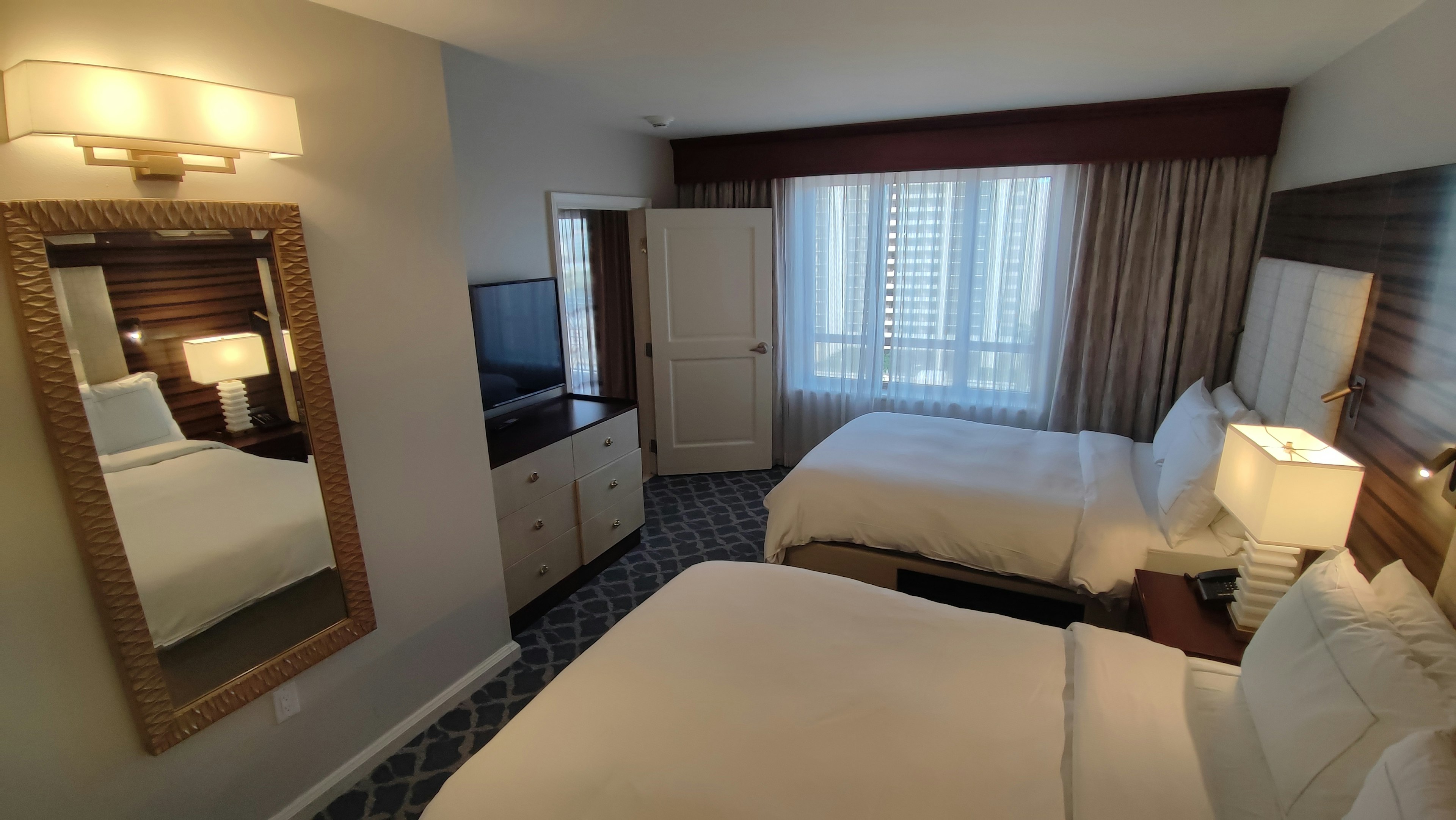 Bright hotel room with two beds large window and a mirror reflecting the space