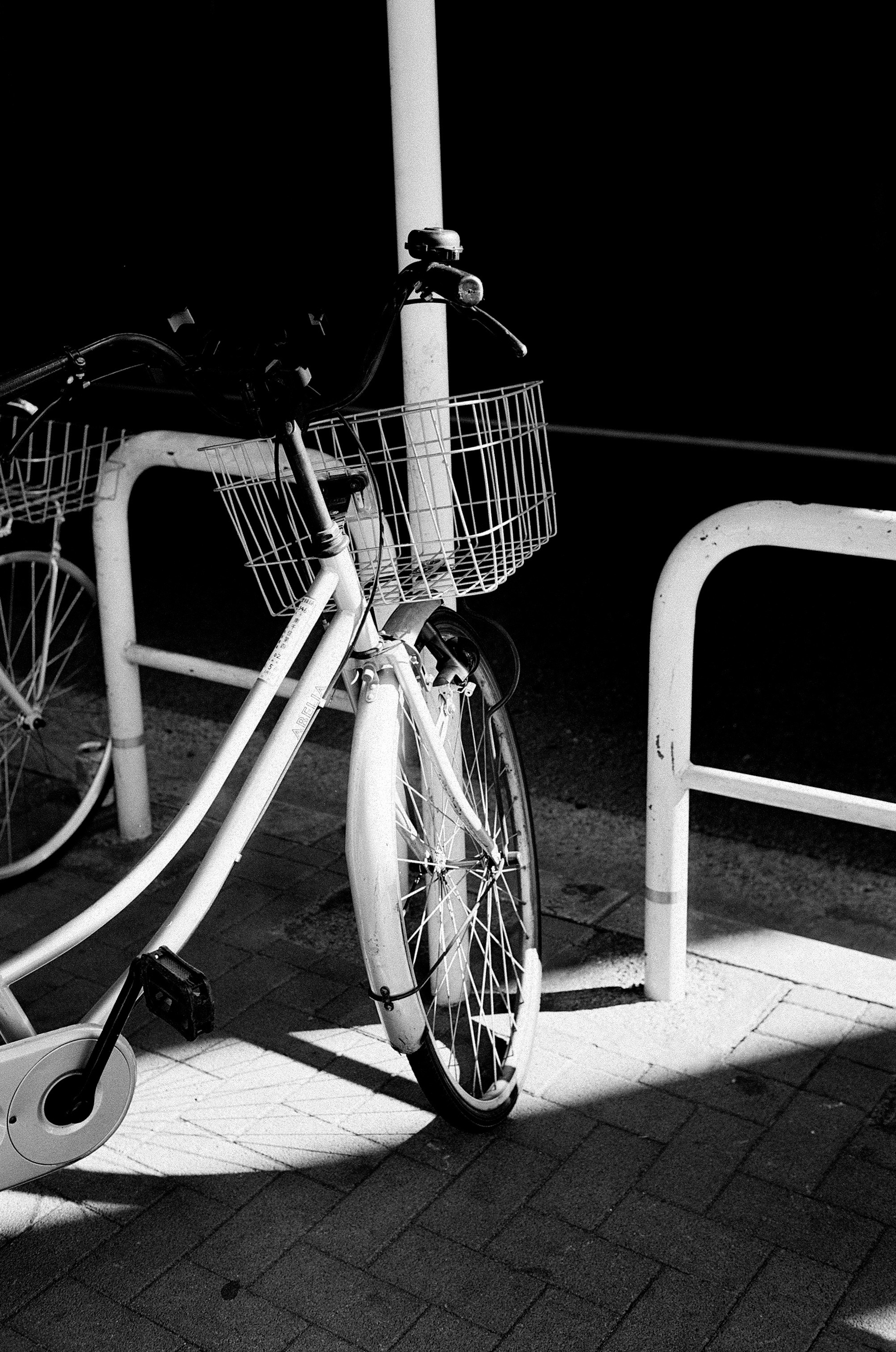 White bicycle with a basket leaning against a railing in low light