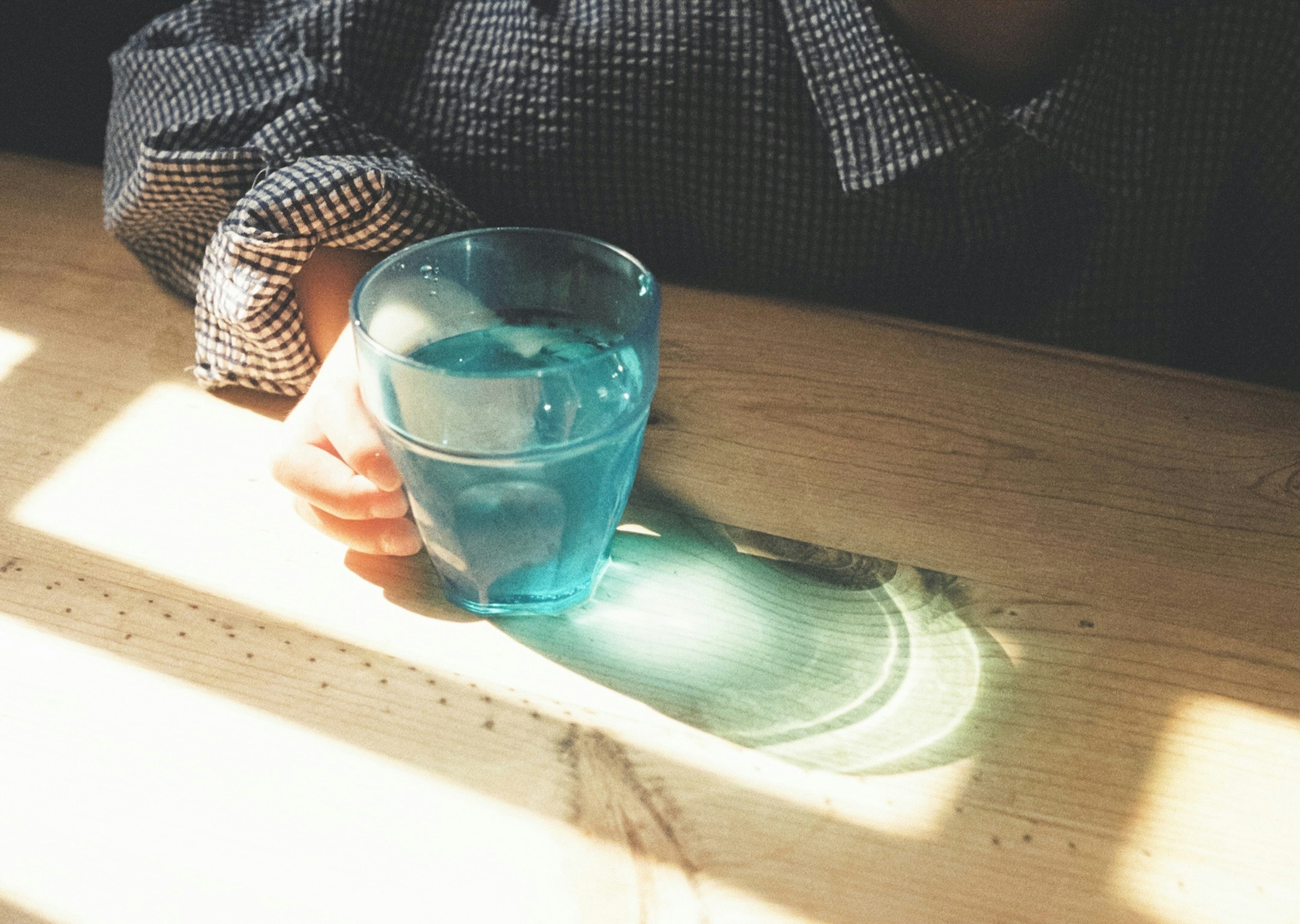 Main tenant un verre bleu sur une table en bois avec des reflets de lumière