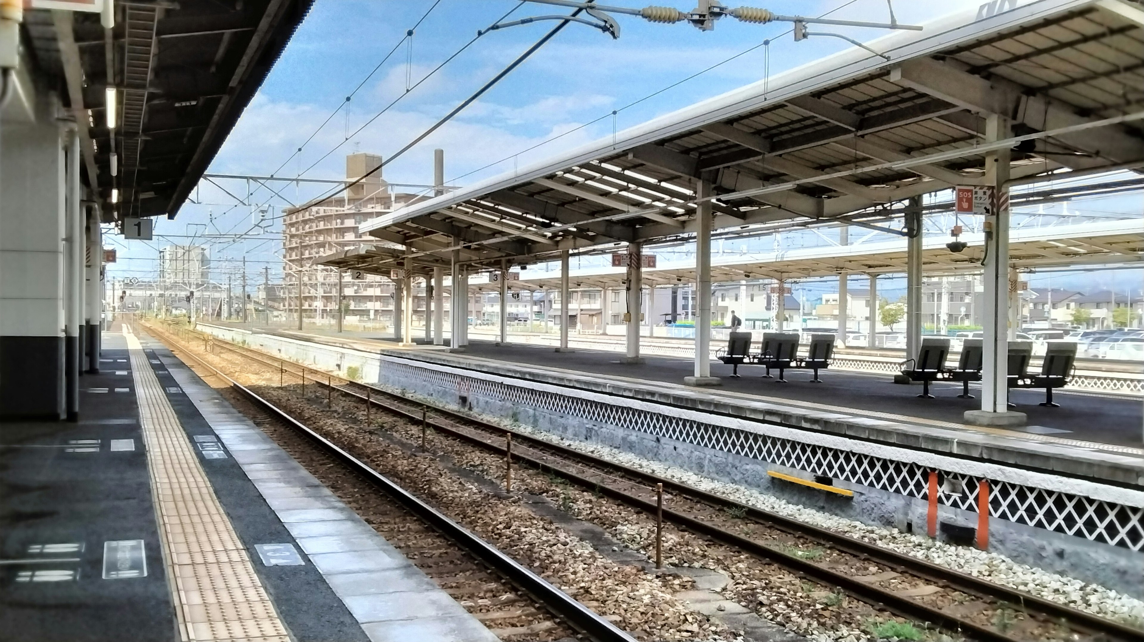 Platform stasiun kereta kosong dengan rel dan bangku terlihat