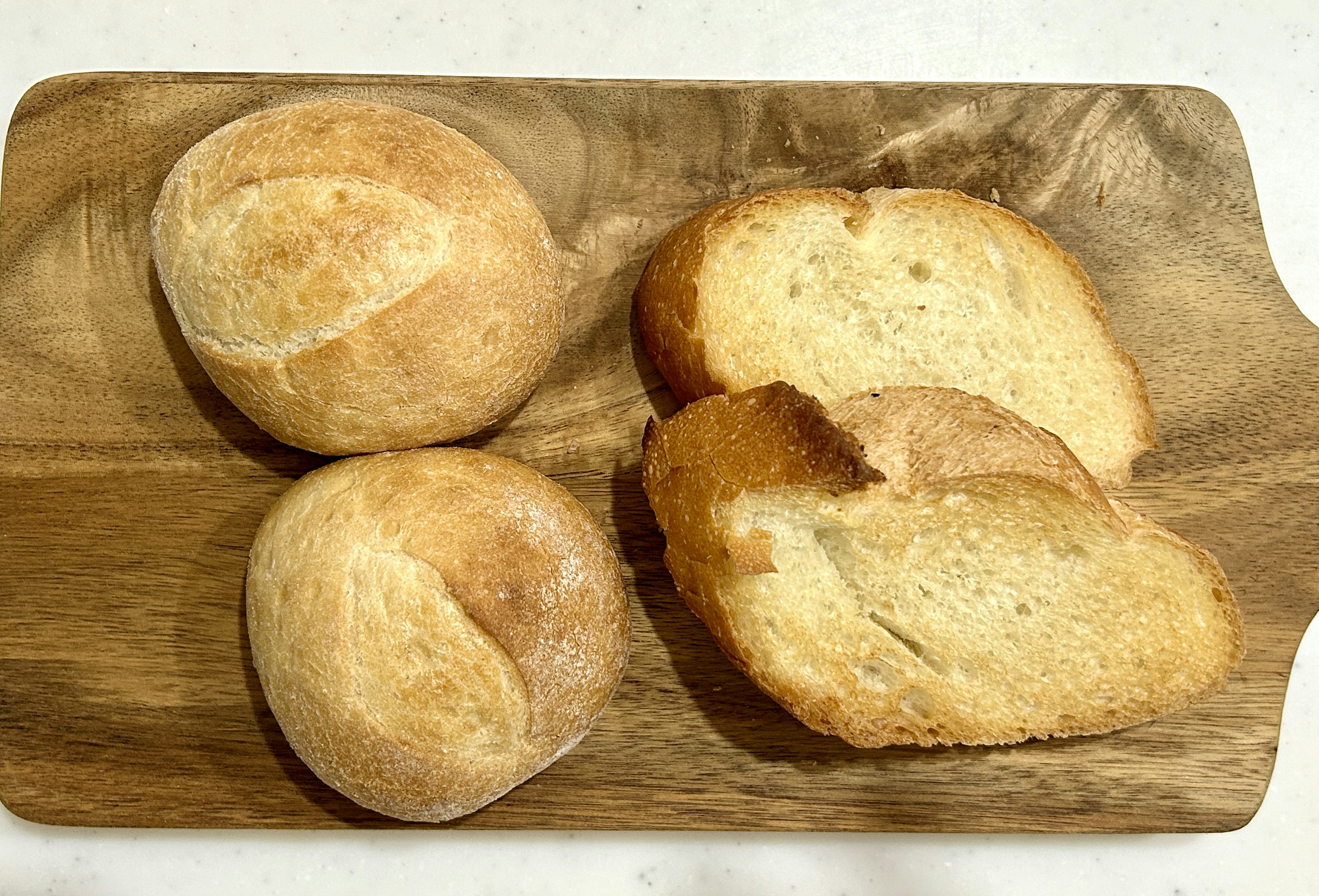 Freshly baked bread rolls and slices on a wooden board