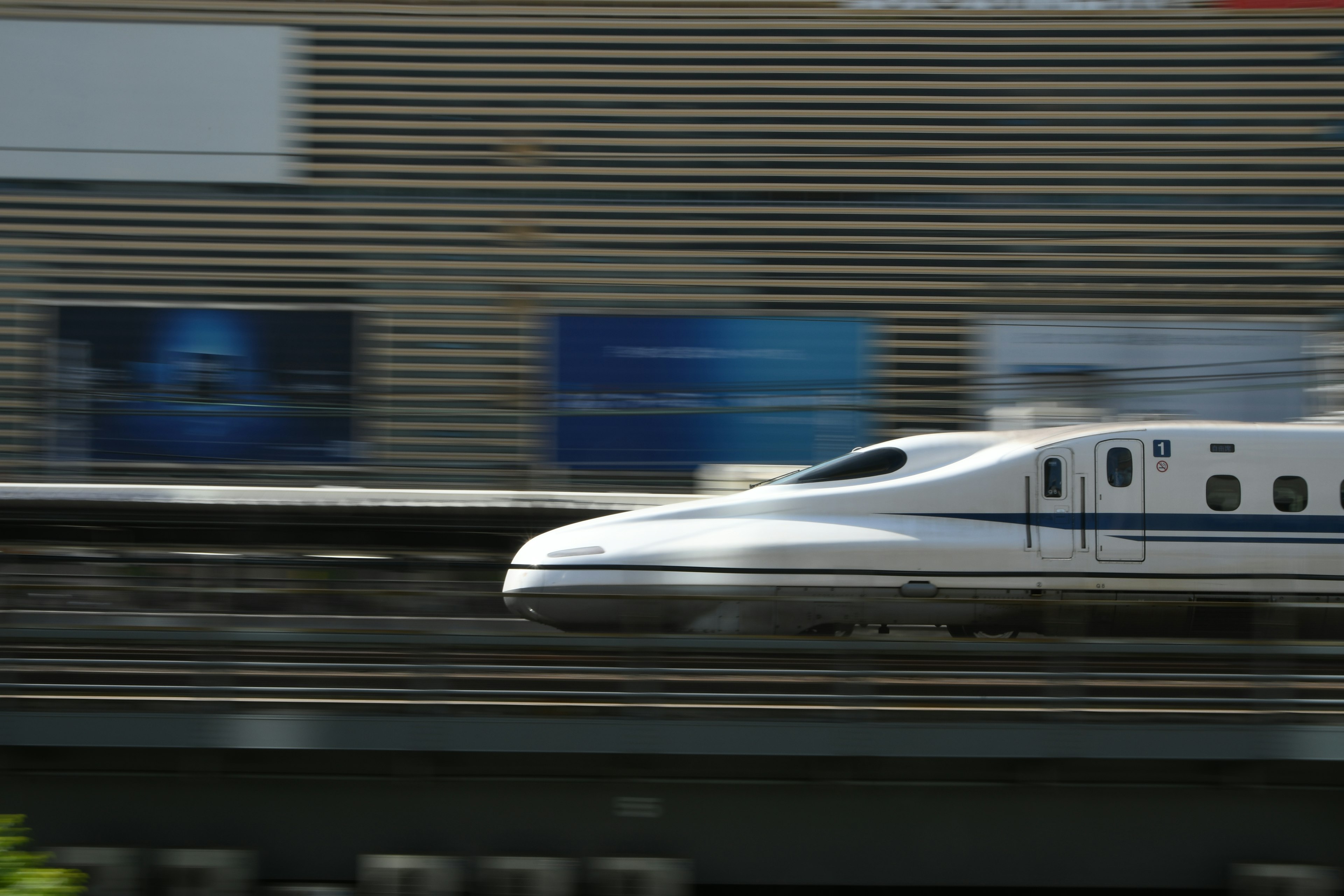 Shinkansen acelerando sobre las vías con anuncios al fondo