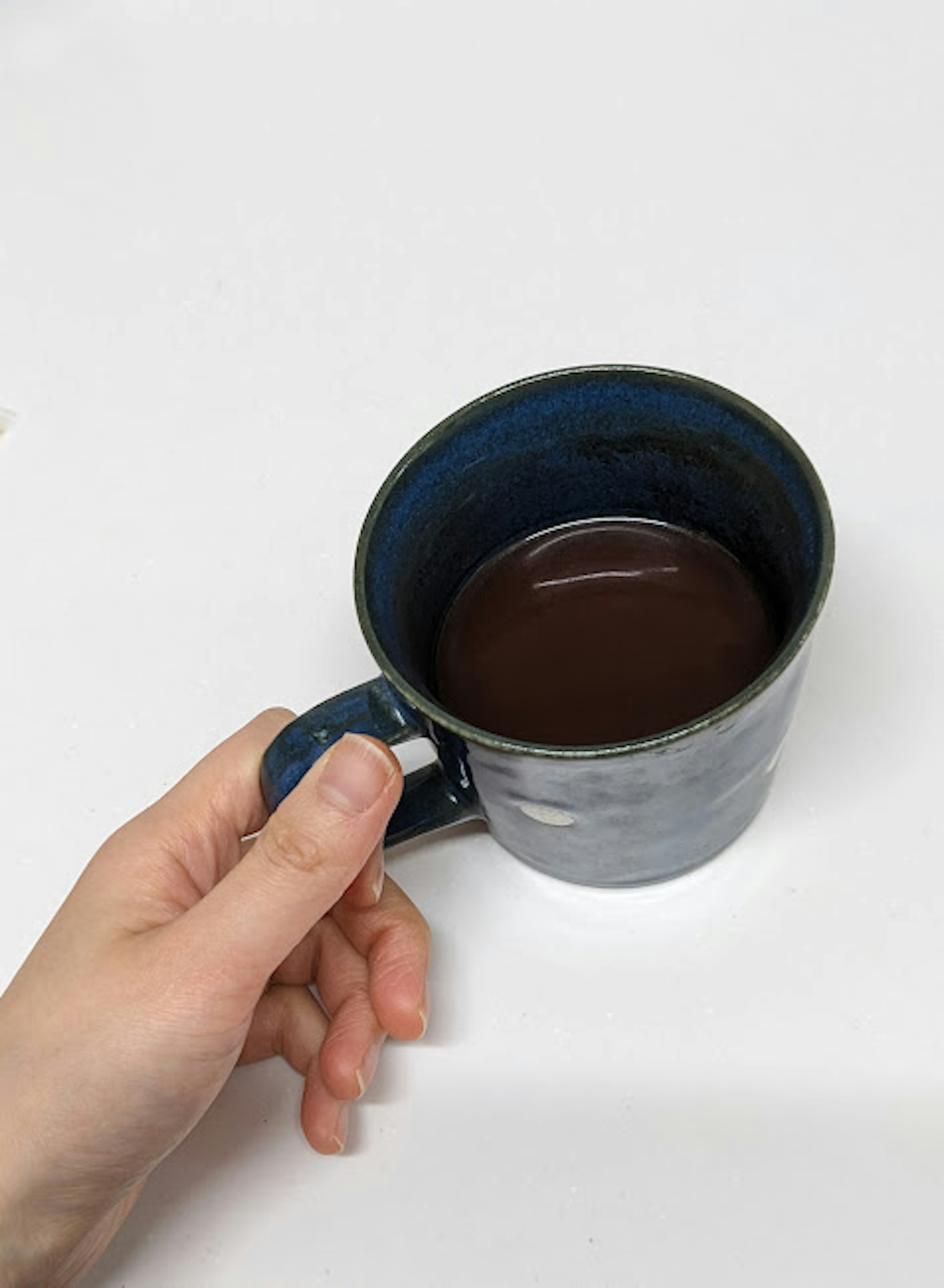 Mano che tiene una tazza di caffè blu riempita di caffè scuro