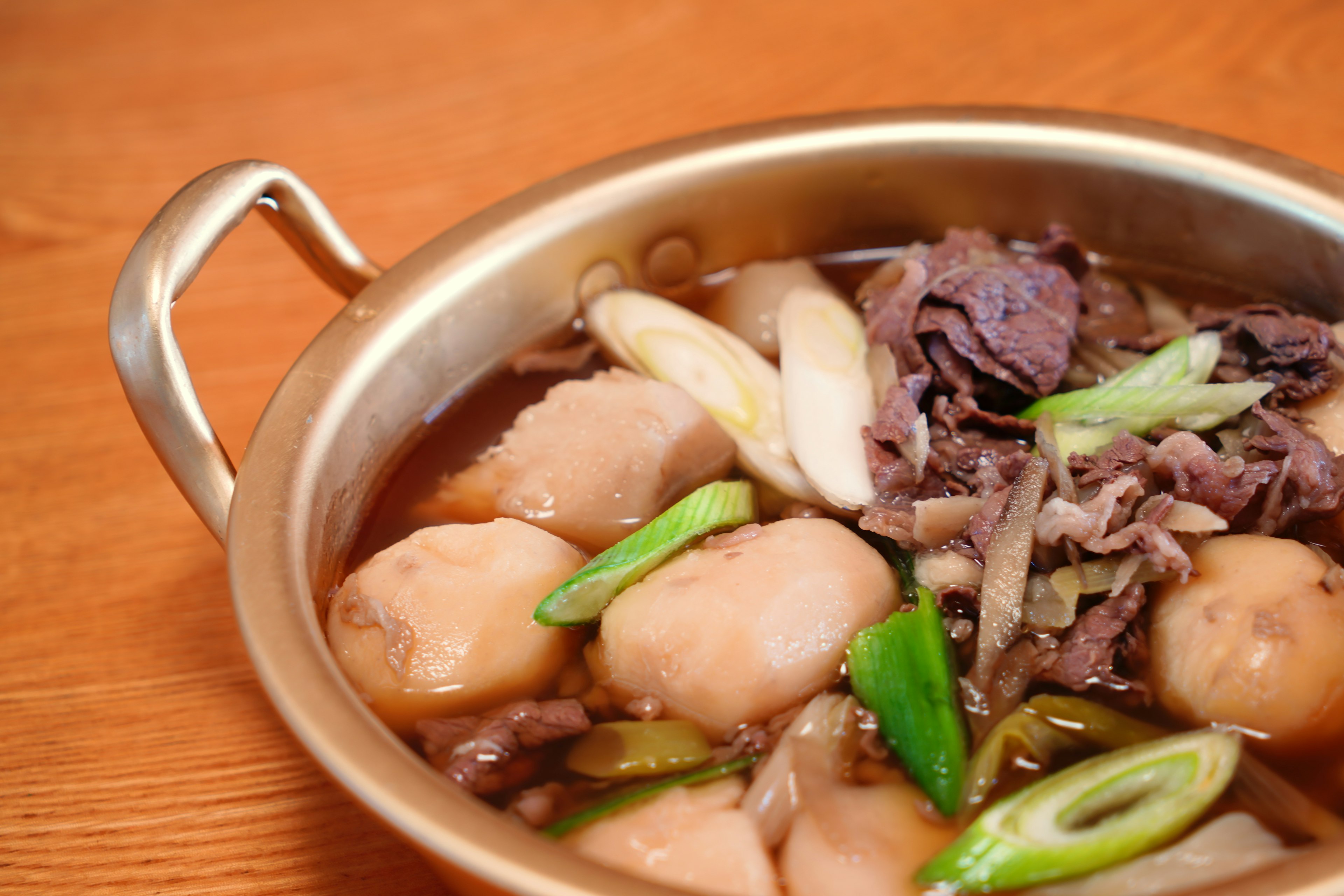 Una olla con carne y cebollas verdes en un caldo sabroso