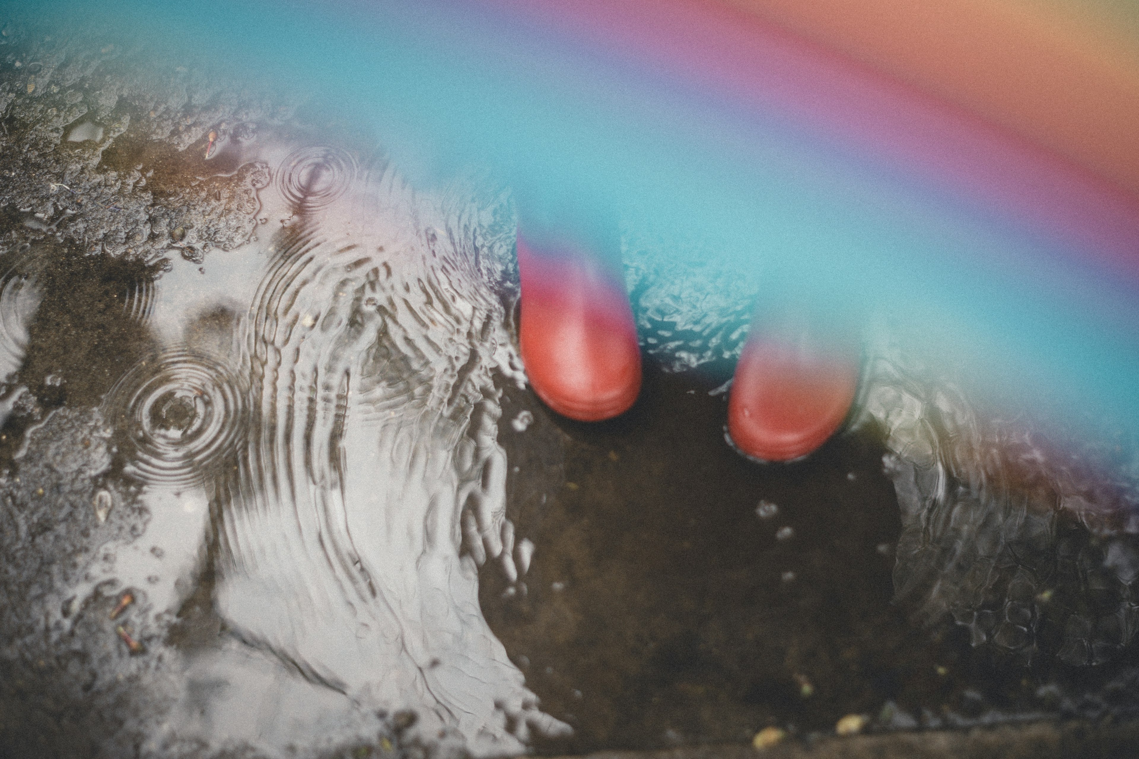 Red rubber boots standing in a puddle with a rainbow arc above