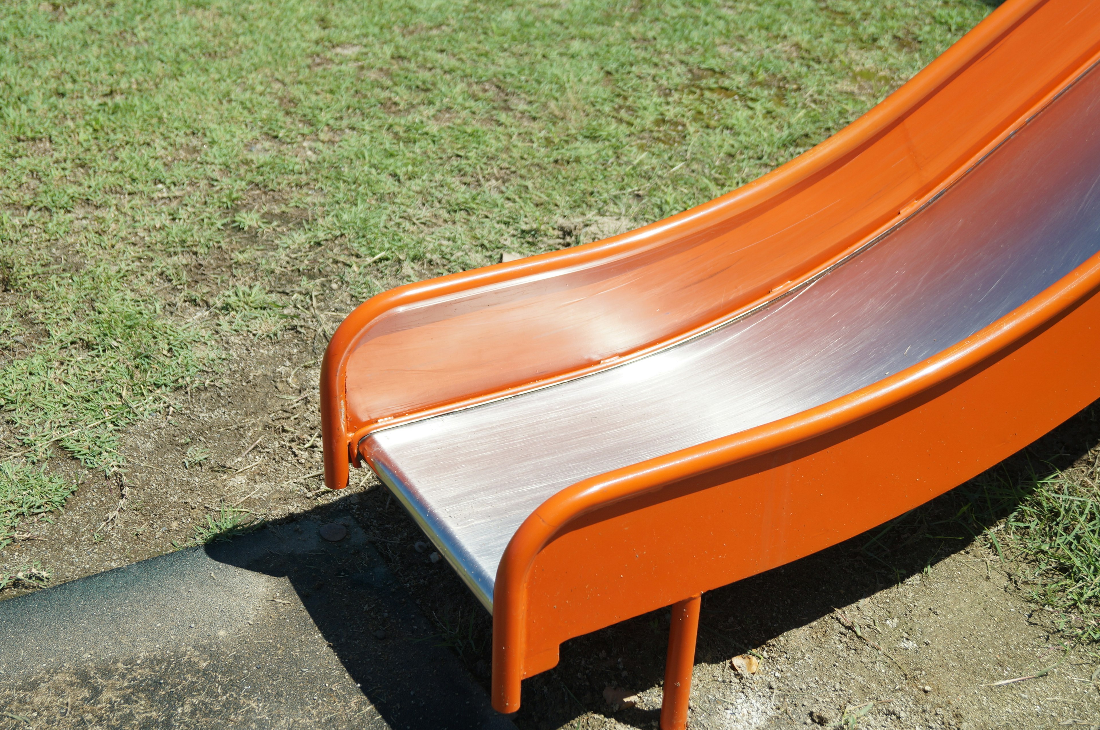 An orange slide with a metallic surface on grassy ground