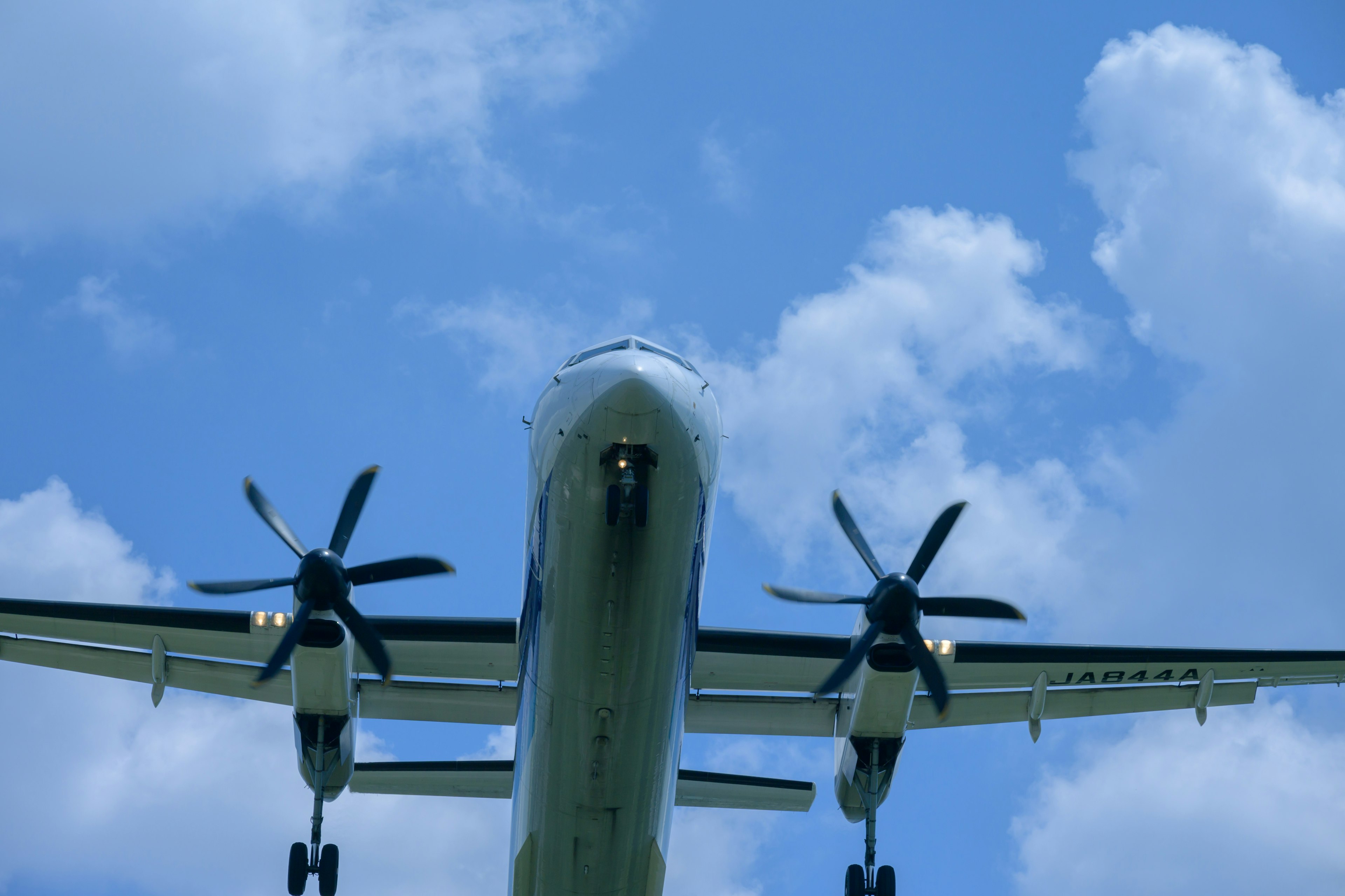 Blick von unten auf ein Propellerflugzeug, das in einem blauen Himmel fliegt