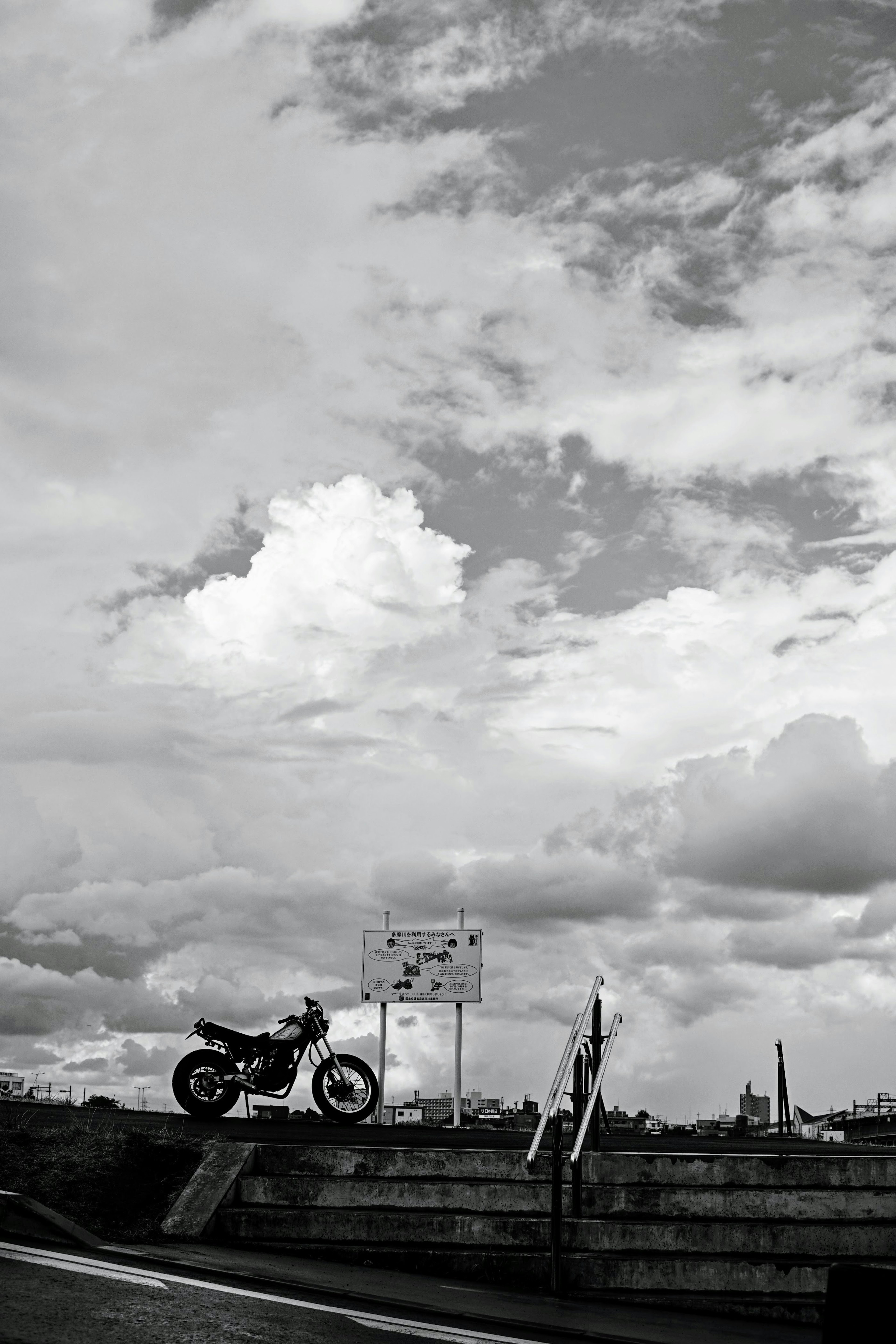 Black and white image of a motorcycle parked against a cloudy sky