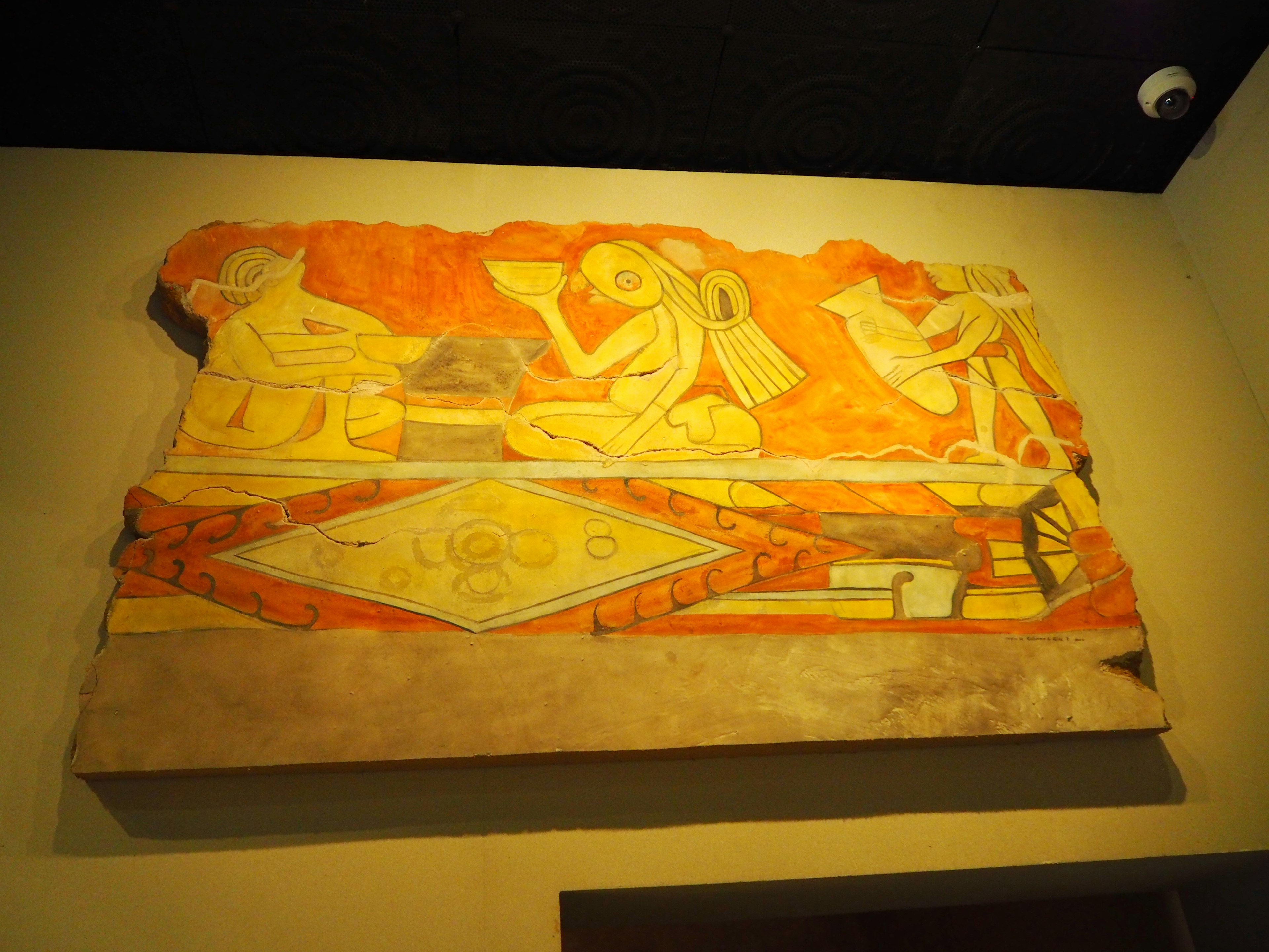 Image of an ancient mural on a stone slab featuring vibrant orange background with figures