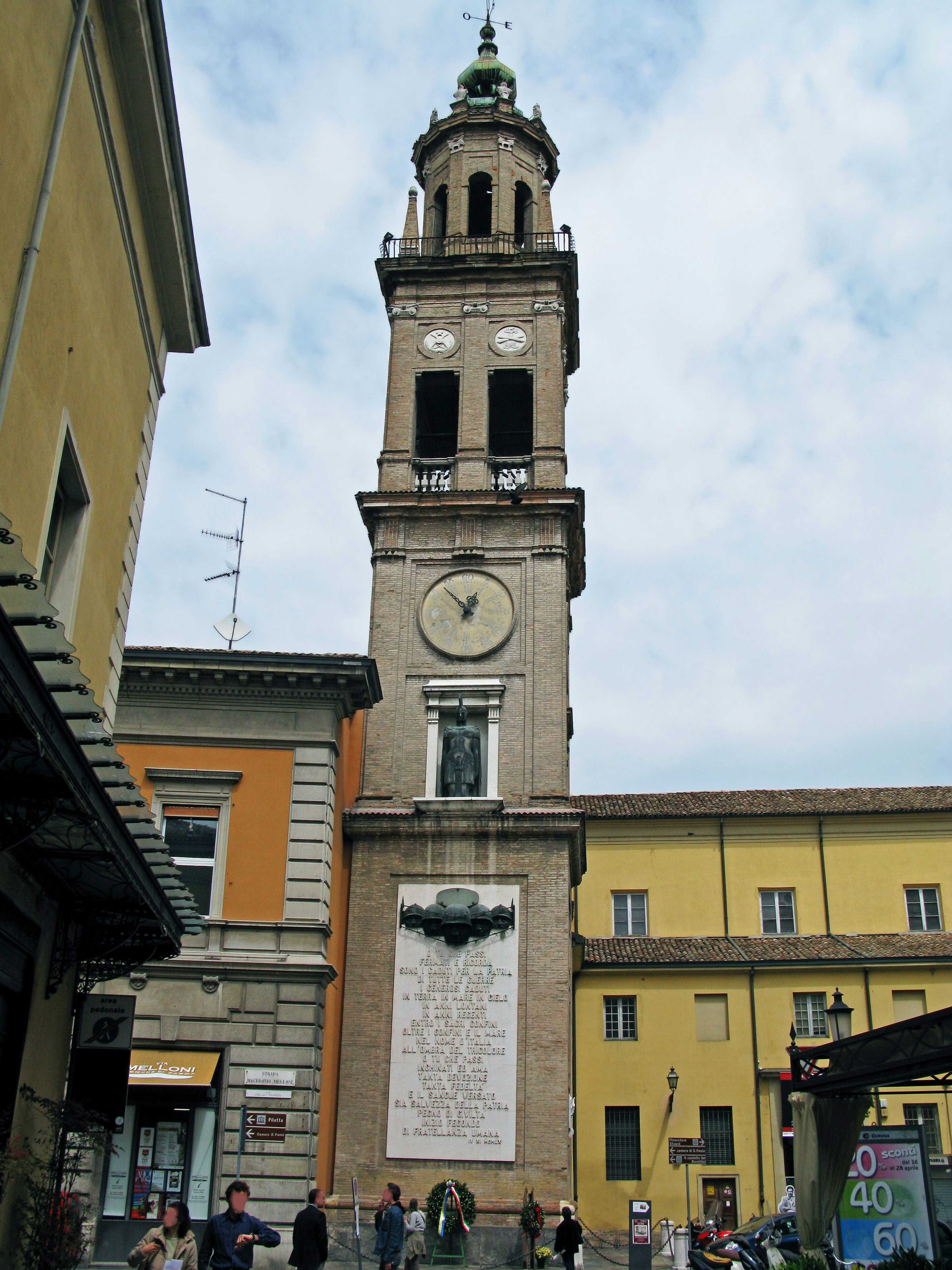 A tall clock tower stands in a square surrounded by colorful buildings