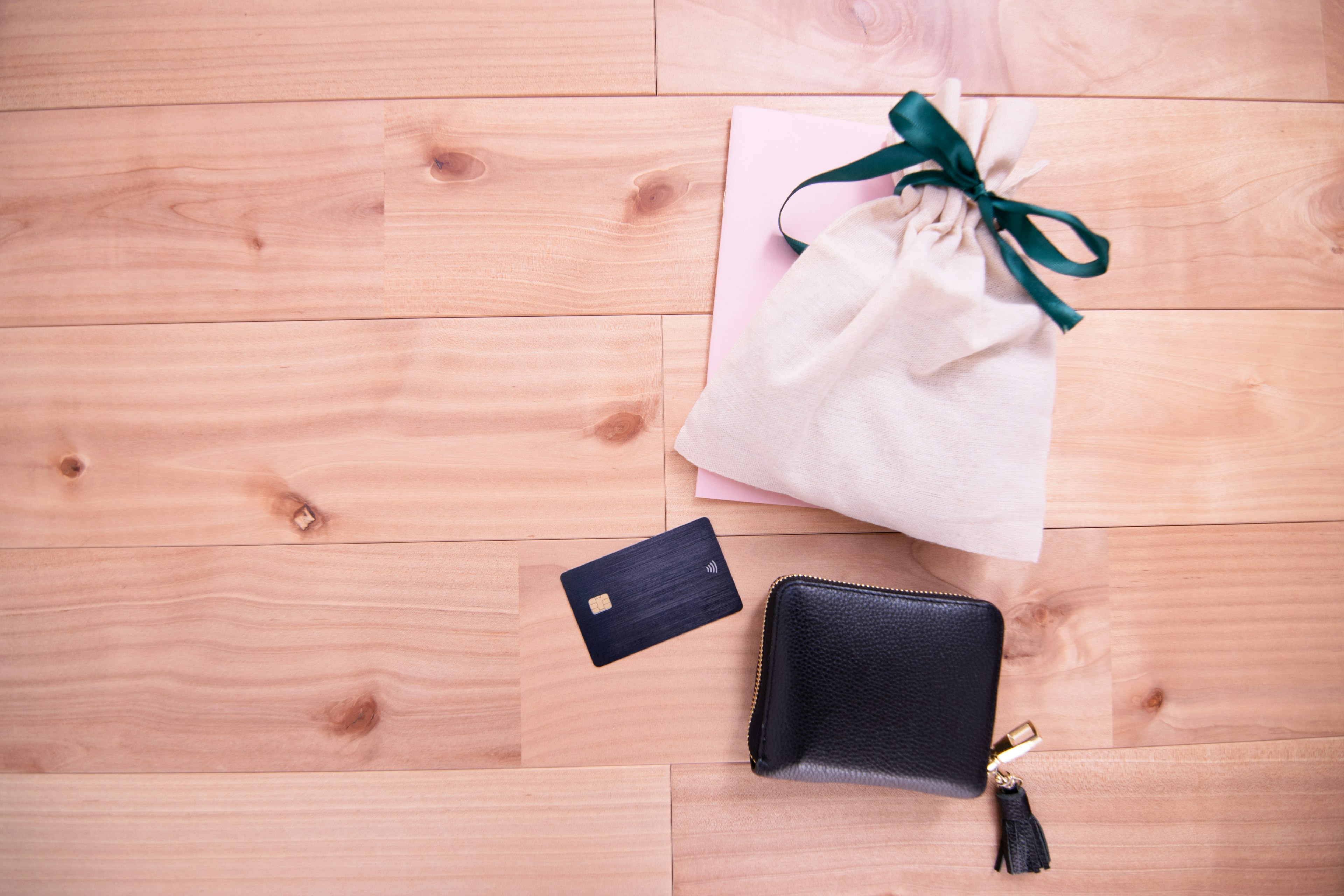 Un portefeuille noir une carte et un sac blanc avec un ruban vert posés sur un sol en bois