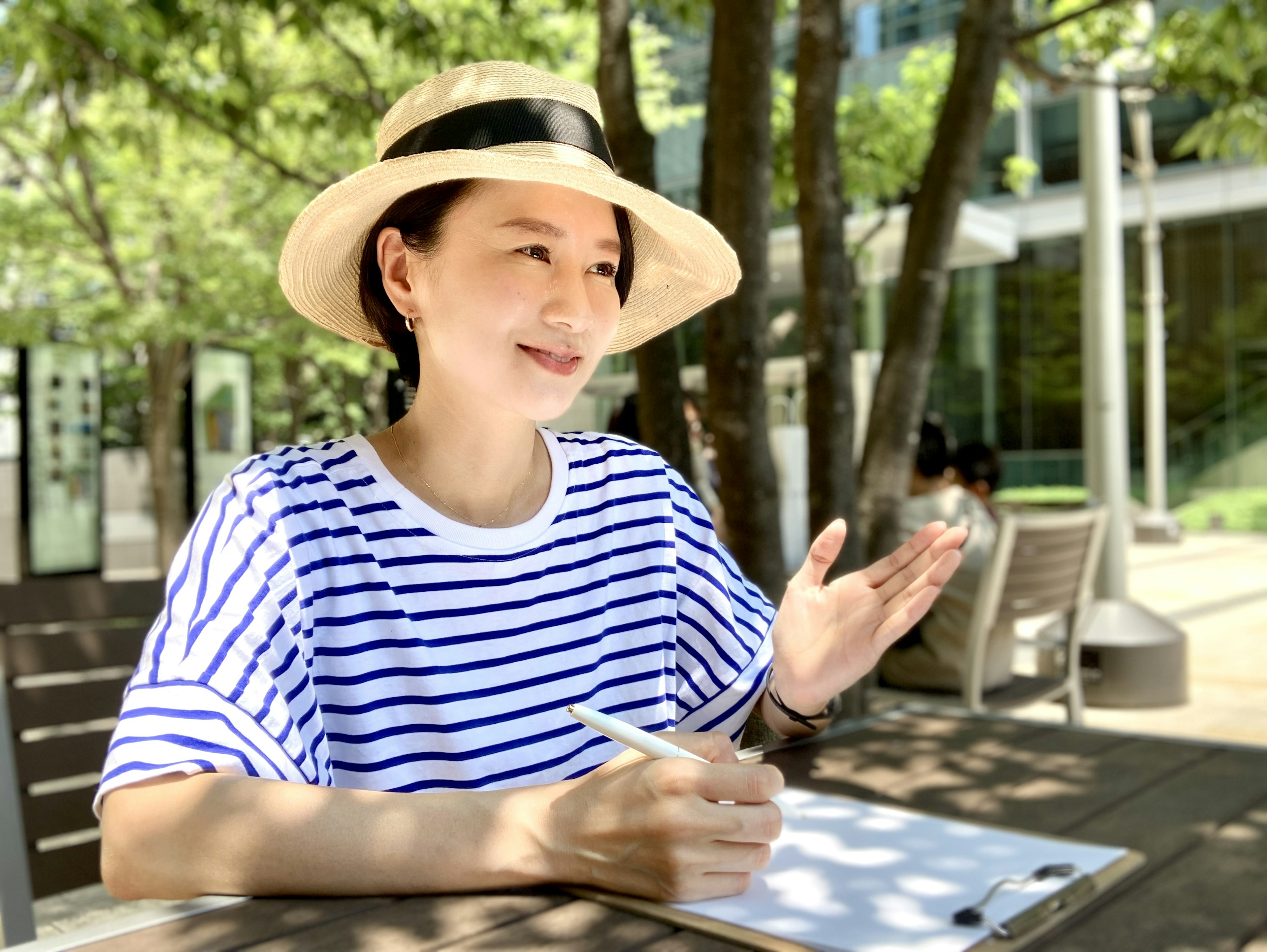 Donna con una camicia a righe e un cappello seduta all'aperto mentre scrive appunti