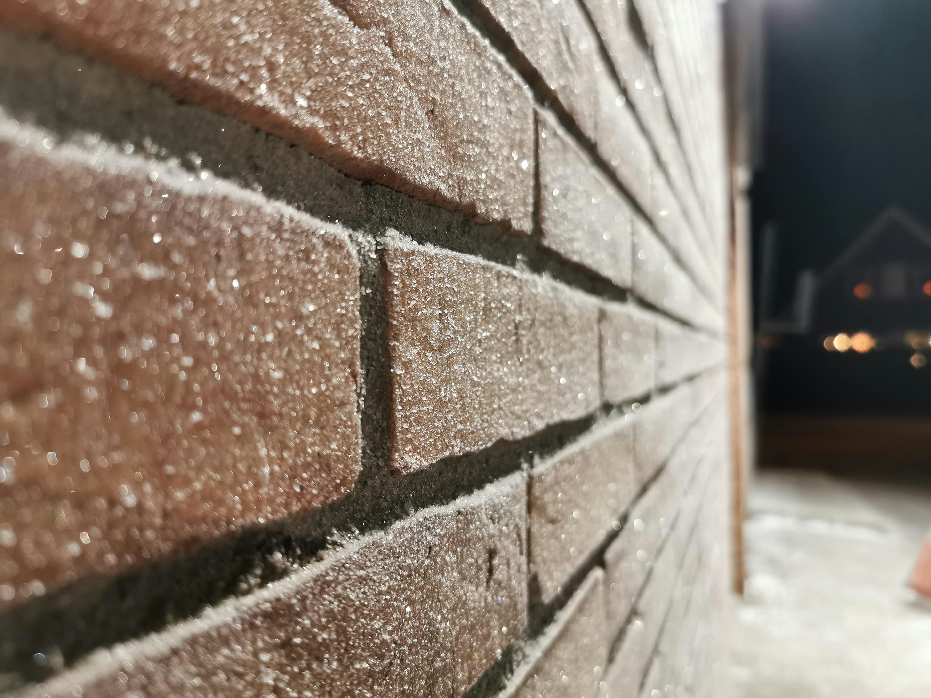 Imagen en primer plano de una pared de ladrillos de noche mostrando textura y luces borrosas de fondo