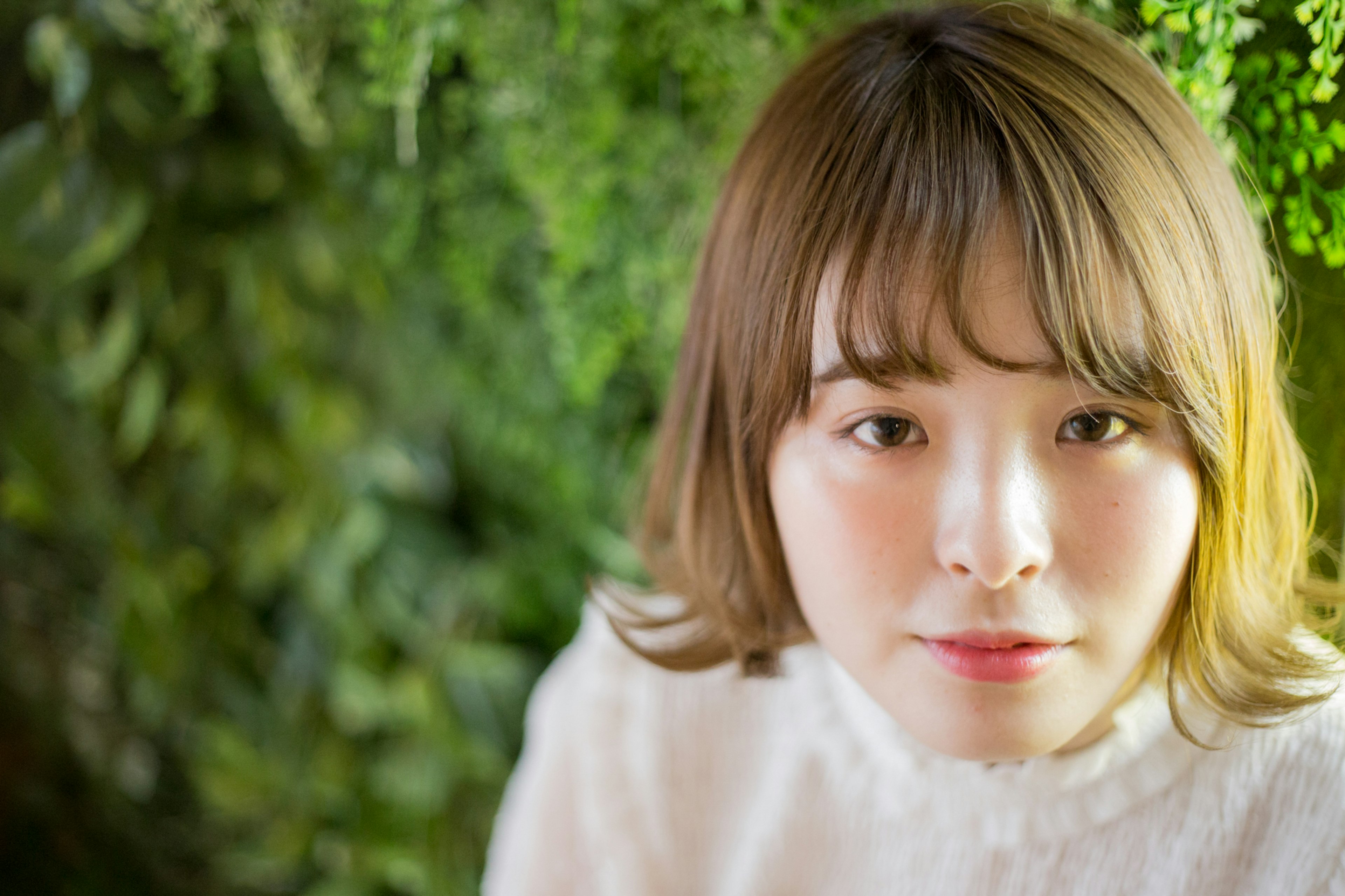 Portrait of a woman in front of a green background wearing a white sweater with light hair