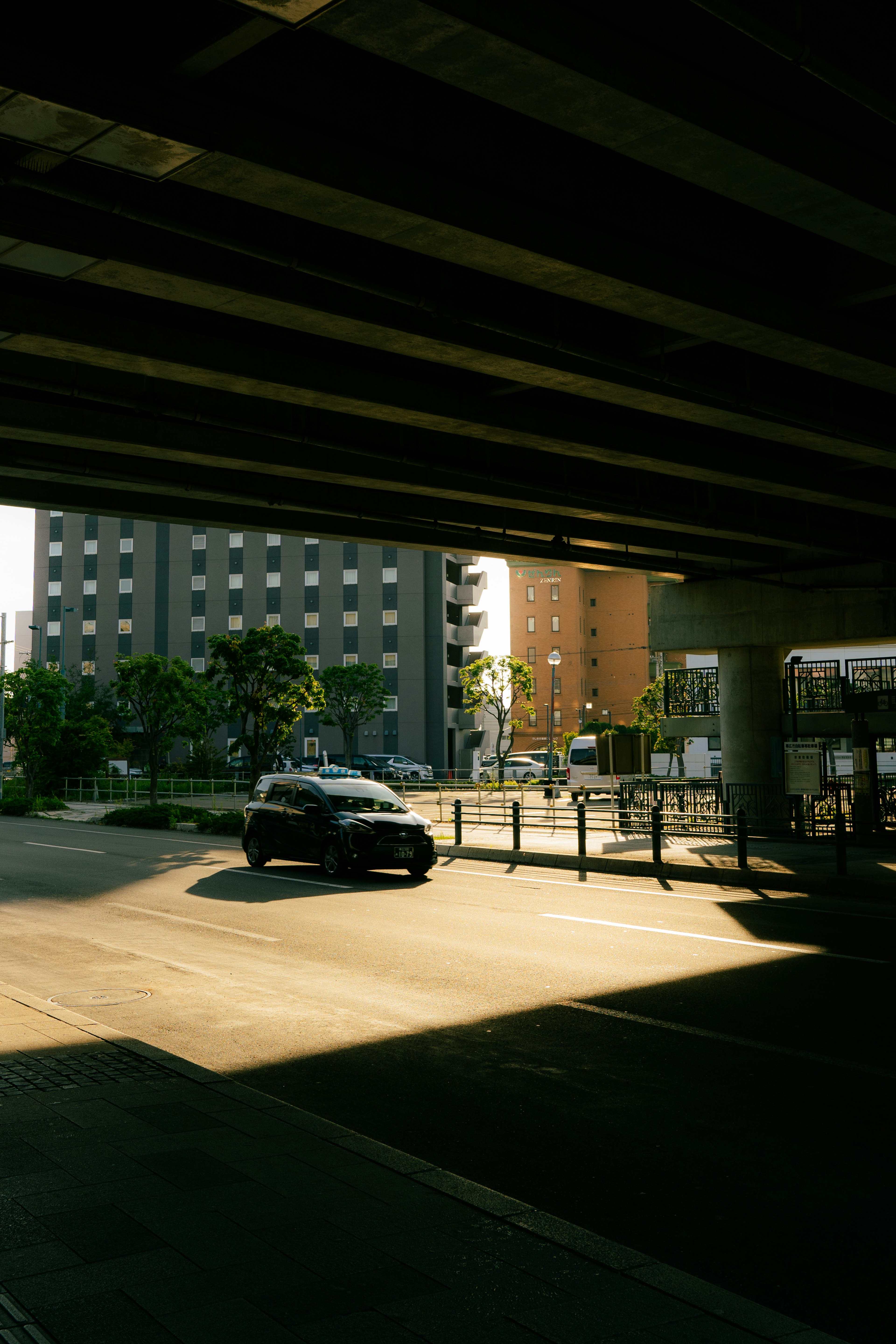 Imagen de un coche negro estacionado en un área de estacionamiento iluminada por el sol bajo un puente