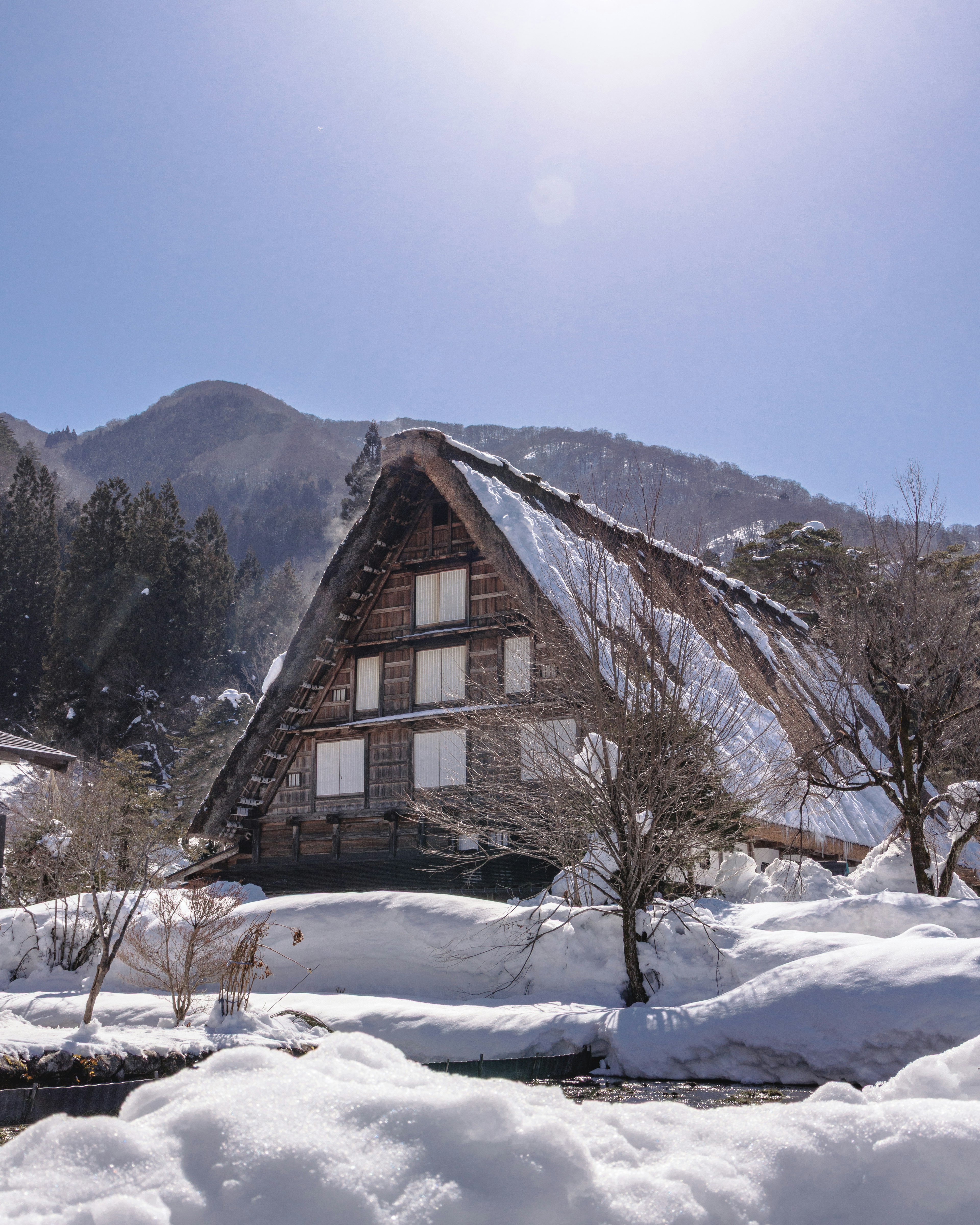 Snow-covered gassho-zukuri house with mountainous background