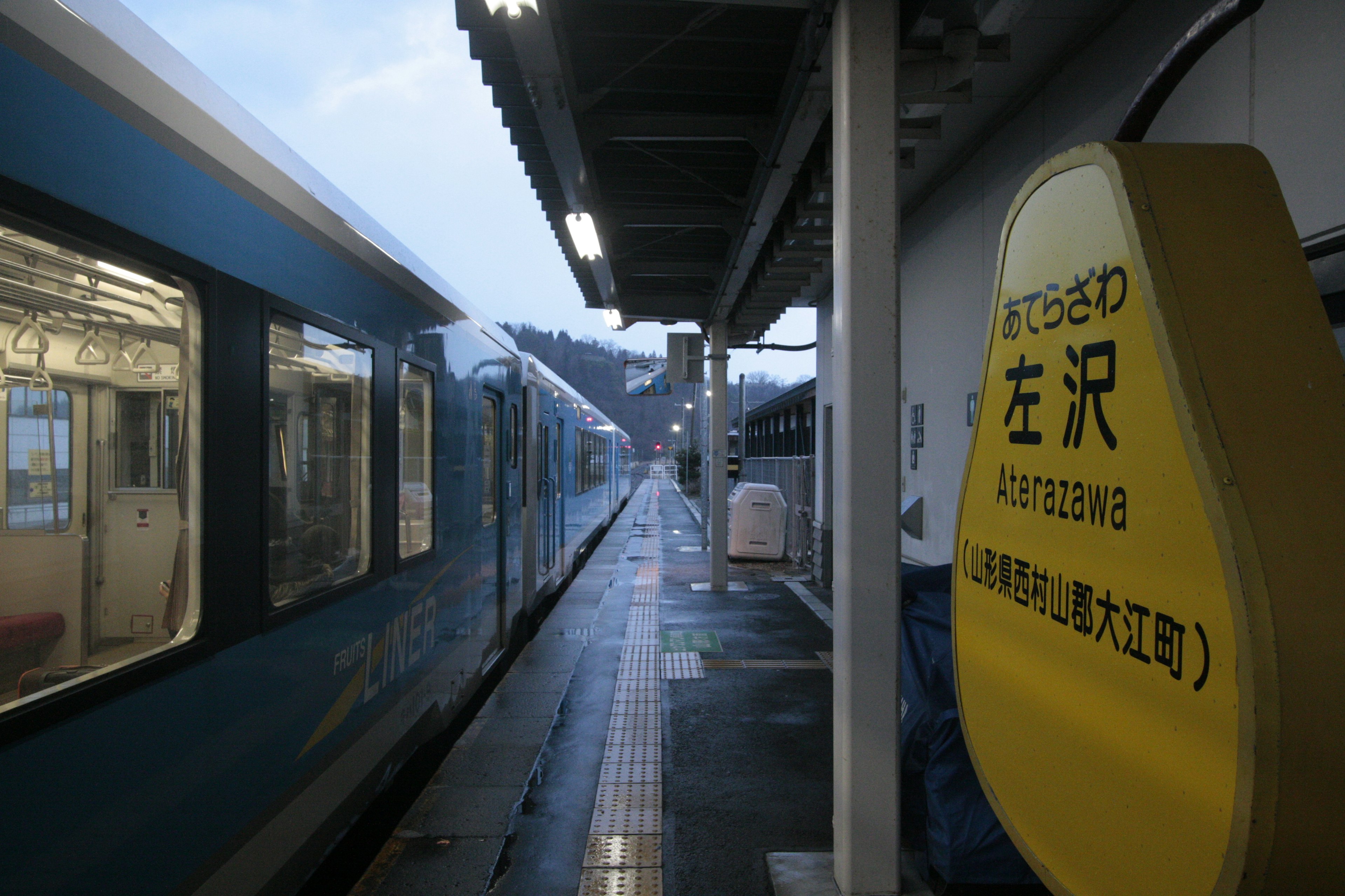 Kereta biru di stasiun hujan dengan papan yang mencolok