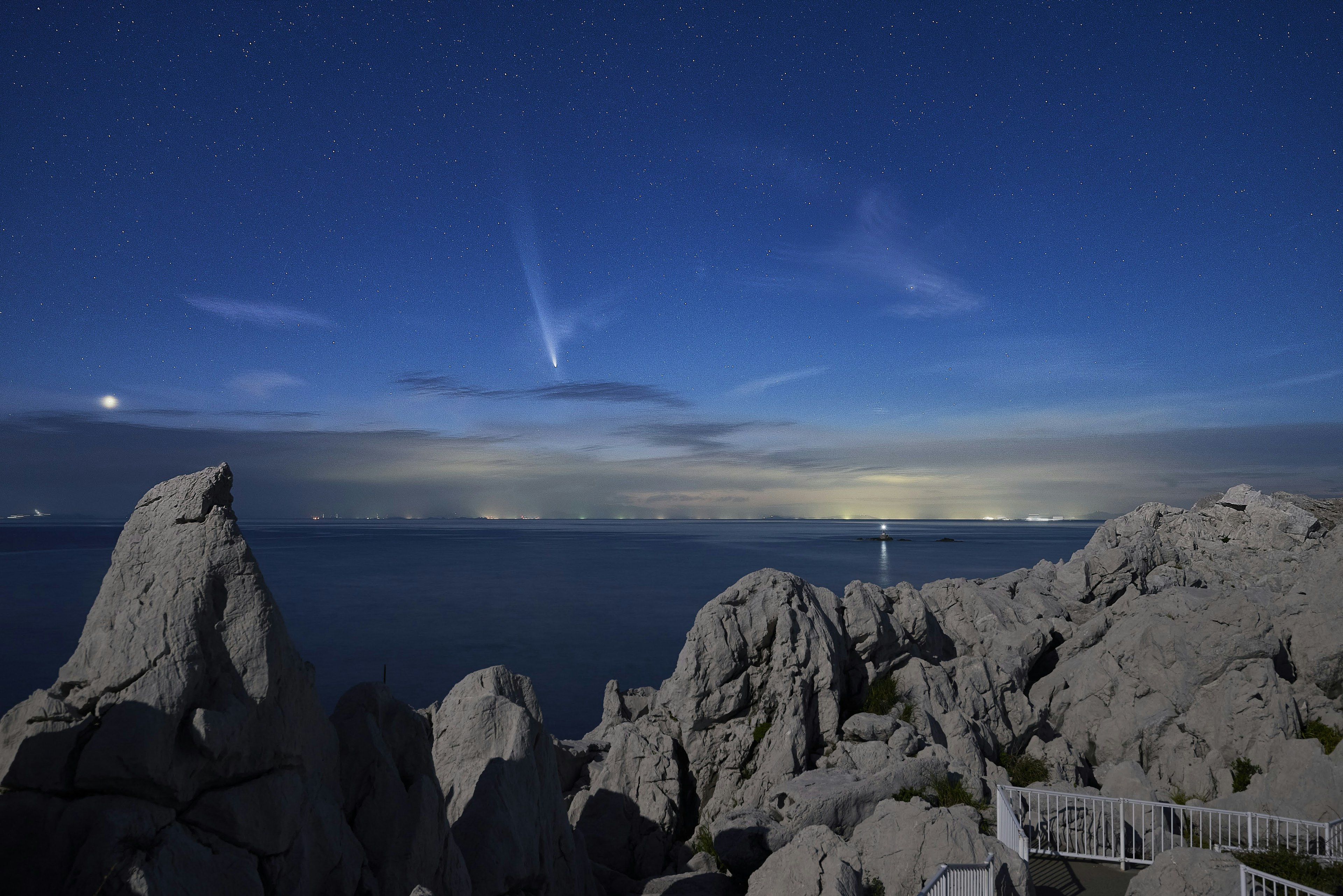 Vista panoramica di una costa rocciosa sotto un cielo stellato con corpi celesti visibili