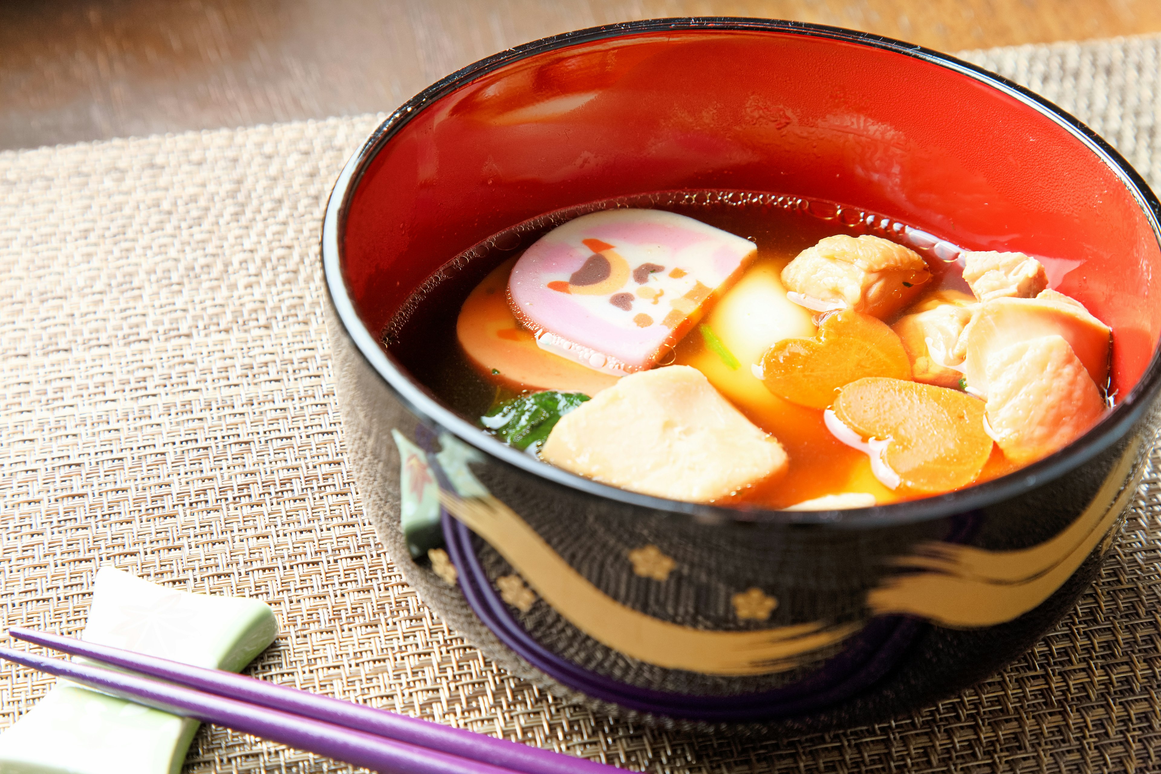 Sopa clara en un tazón rojo con ingredientes coloridos flotantes