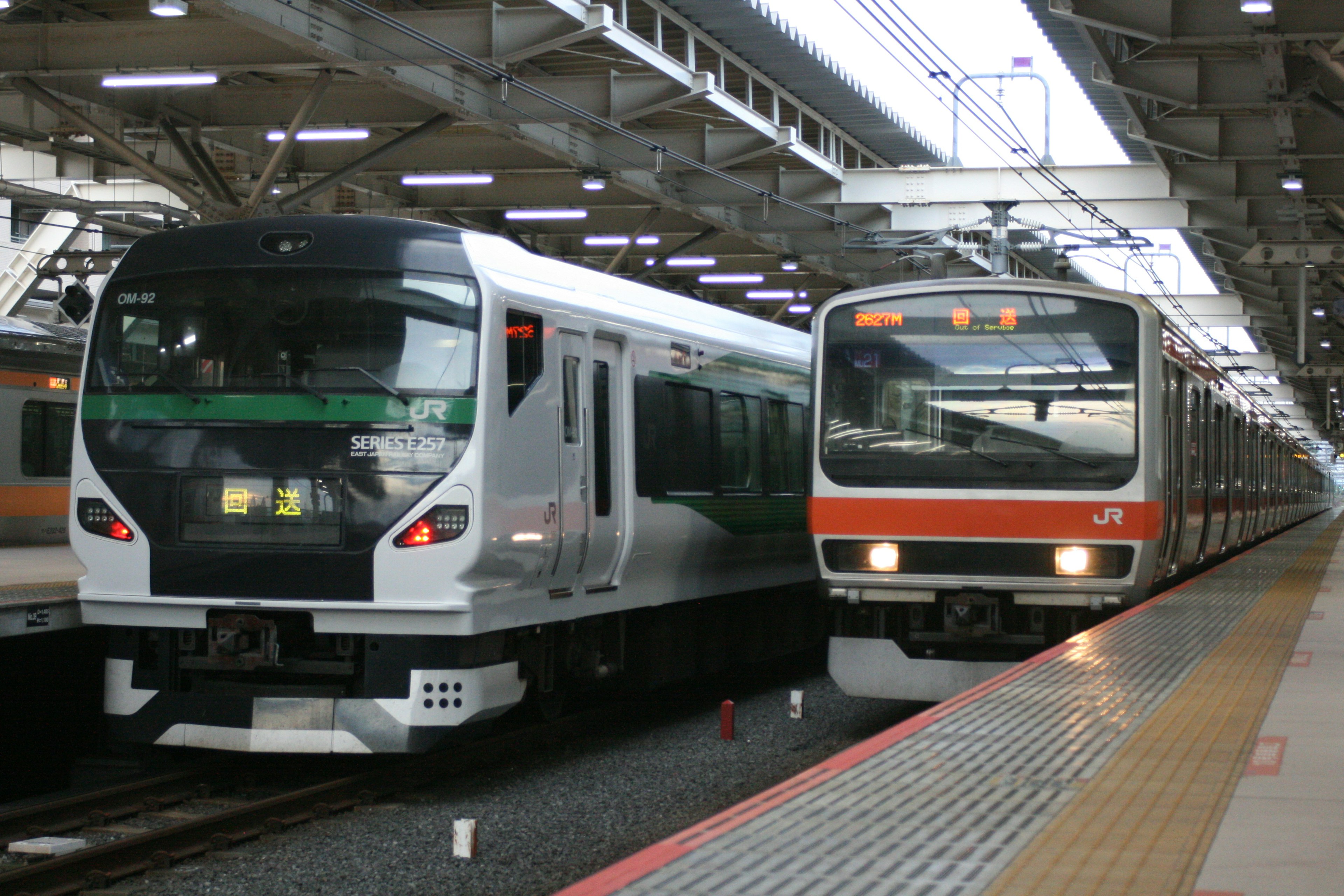 Bild von zwei Zügen an einem Bahnhof ein weißer Zug und ein orangefarbener Zug nebeneinander