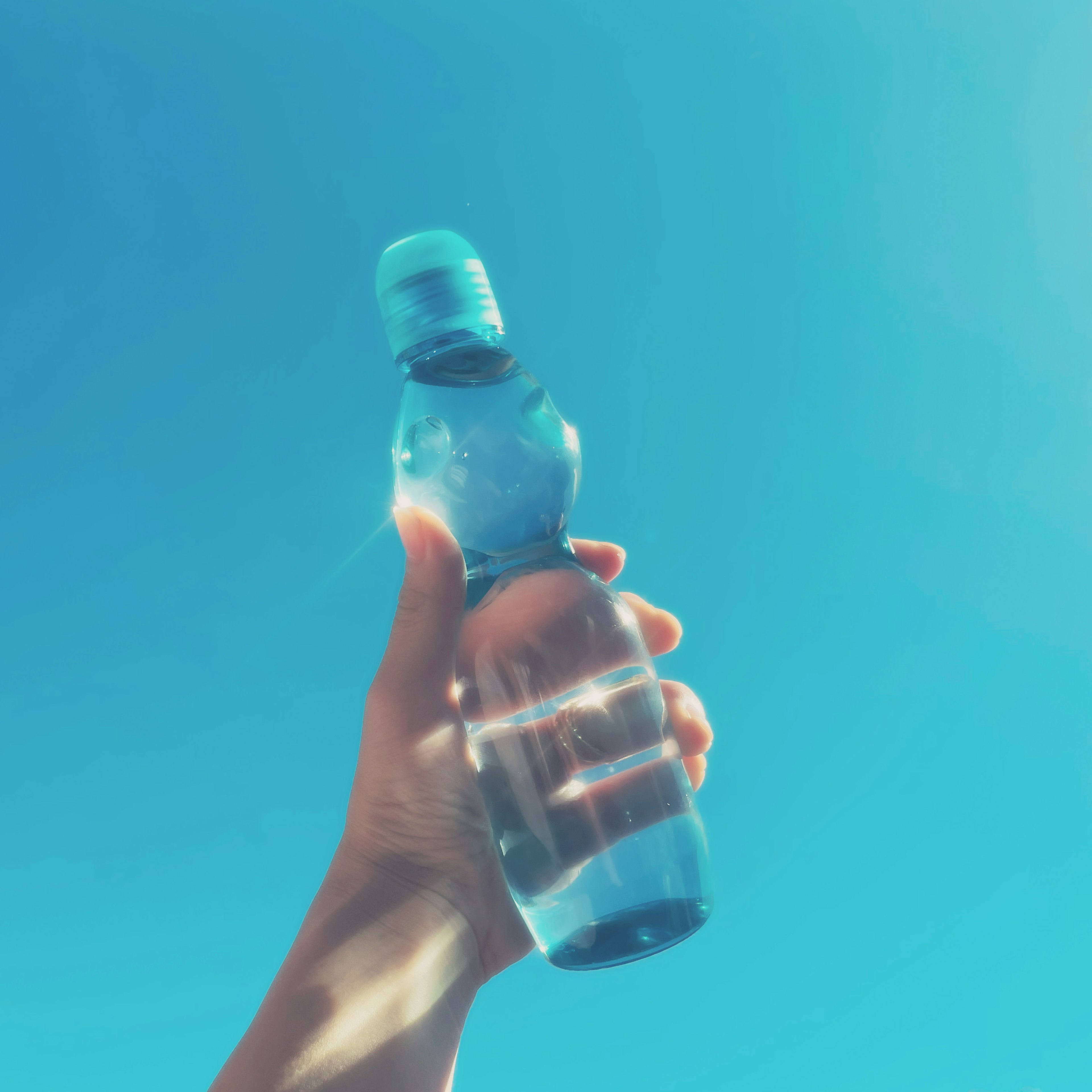 Hand hält eine Wasserflasche vor einem klaren blauen Himmel